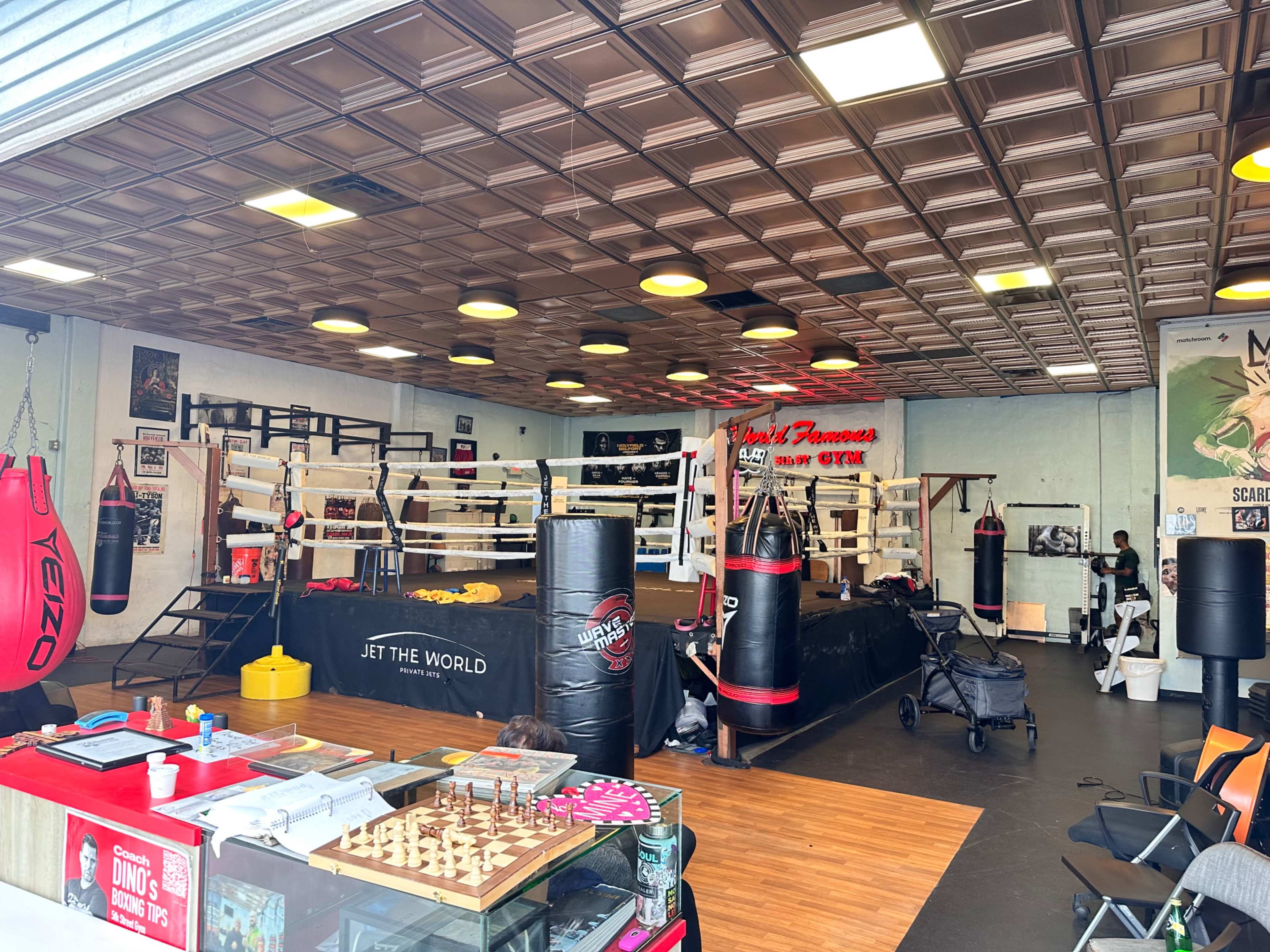 A boxing gym with a central ring, surrounded by punching bags and training equipment.