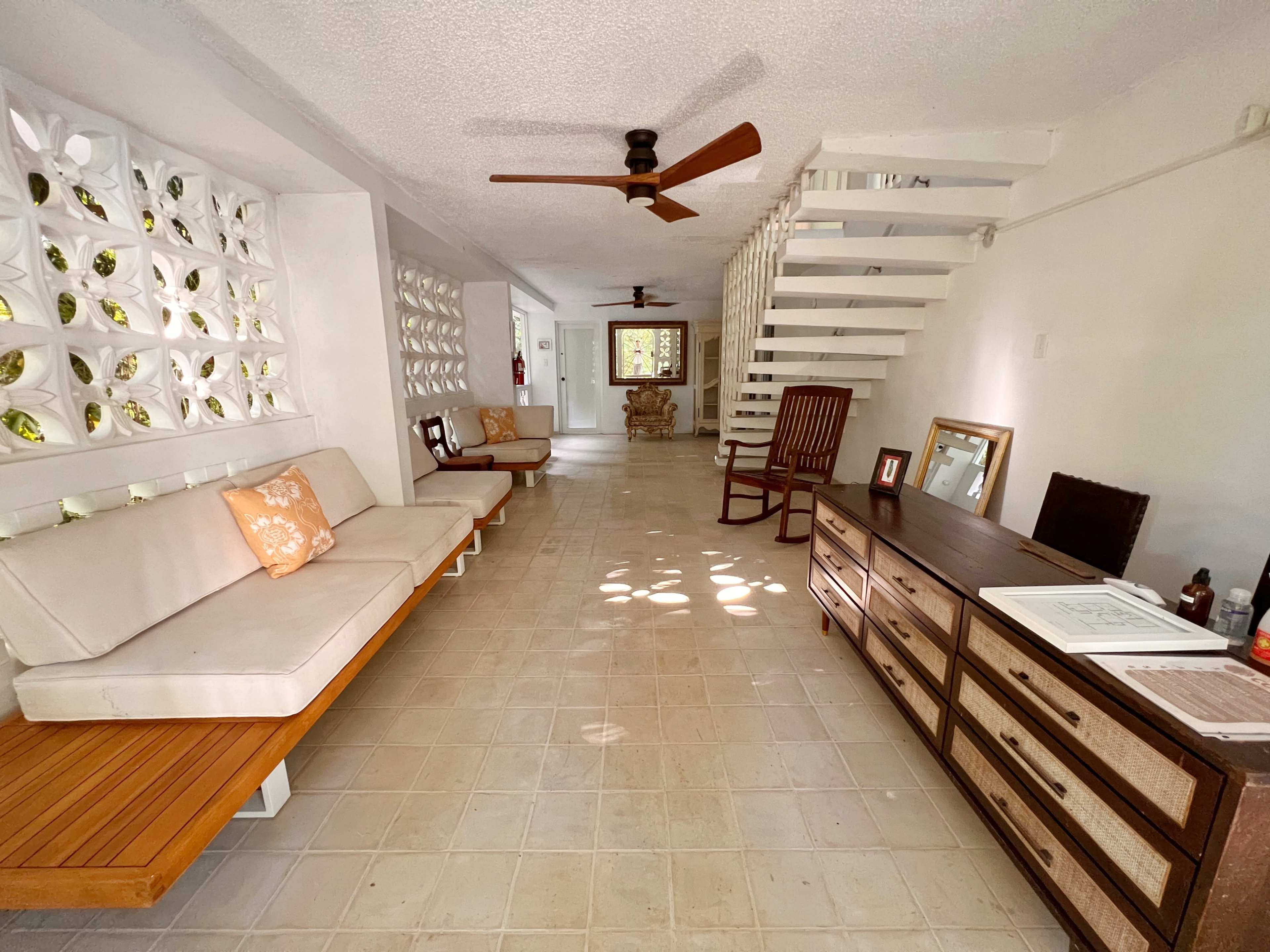 The image shows a spacious hallway with light-colored walls, wooden furniture, and a staircase leading to an upper level.