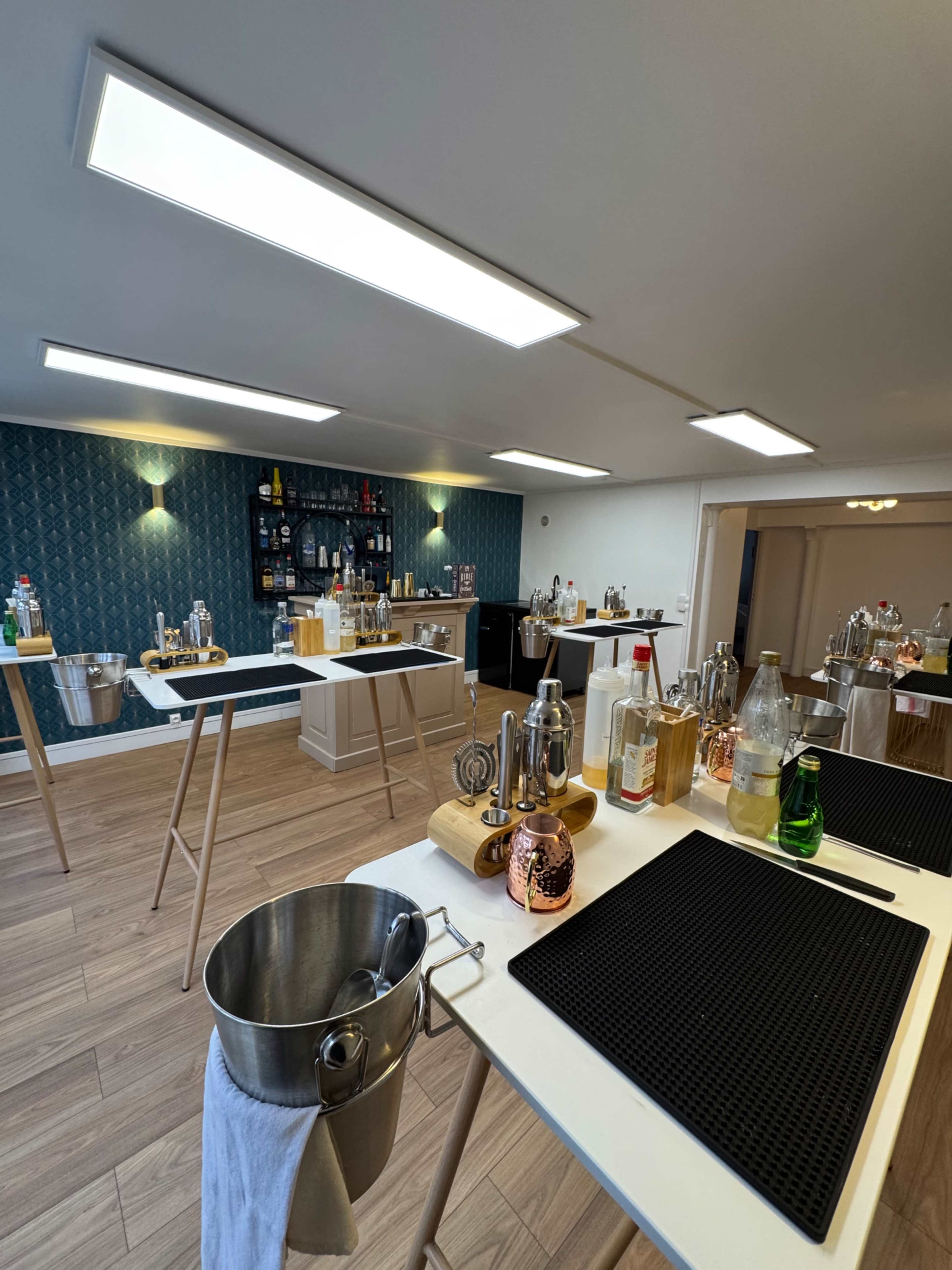 The image shows a well-lit bar setup with multiple cocktail stations equipped with various bottles, mixers, and bar tools on display.