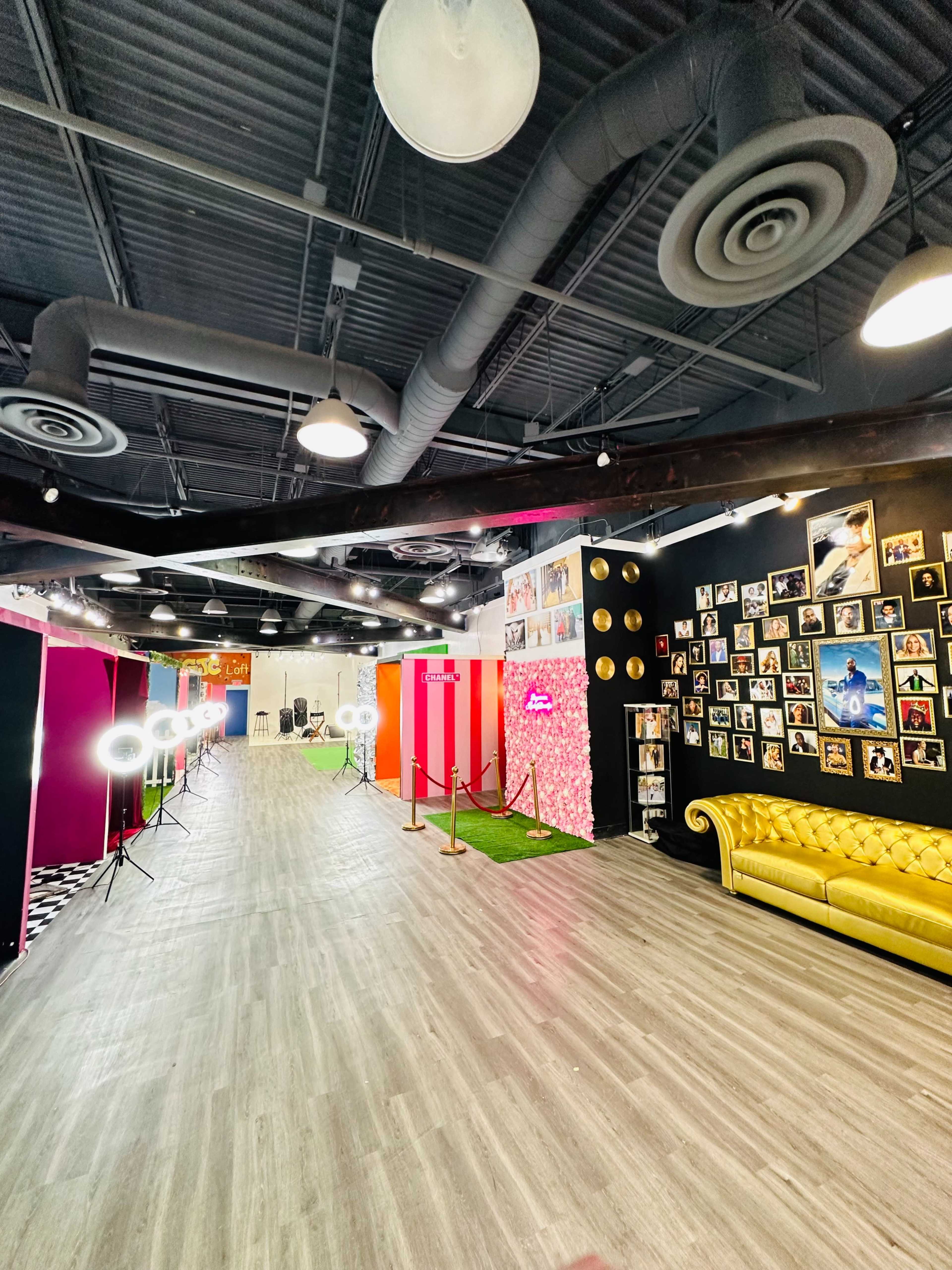 A spacious event venue featuring a yellow couch, photo booths with colorful backdrops, and a gallery wall of framed photos.