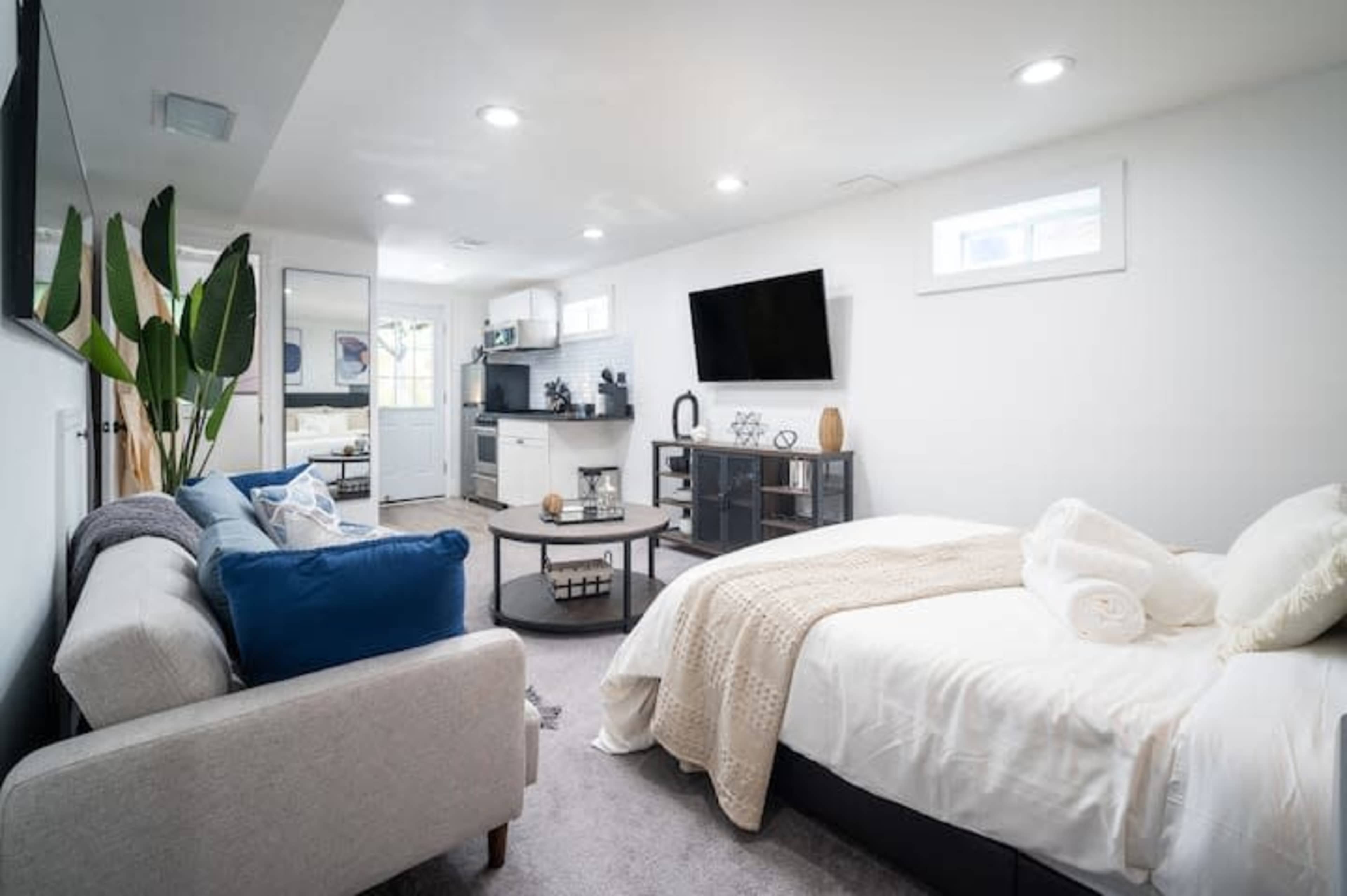 A cozy basement studio apartment featuring a bed, sofa, kitchenette, and a small dining area.