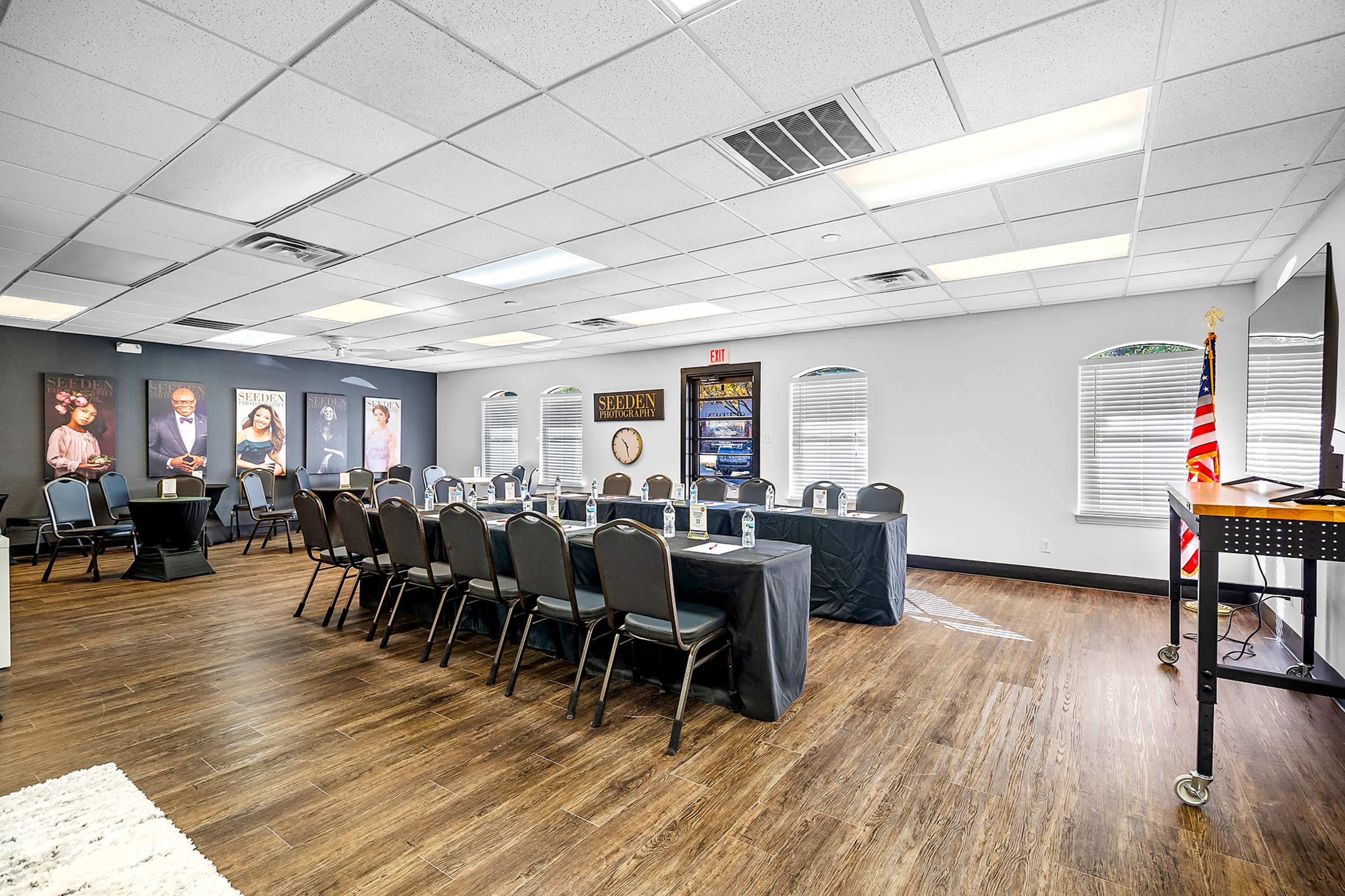 A meeting room arranged with a long, black table set for discussion, surrounded by chairs and featuring framed portraits on the walls.