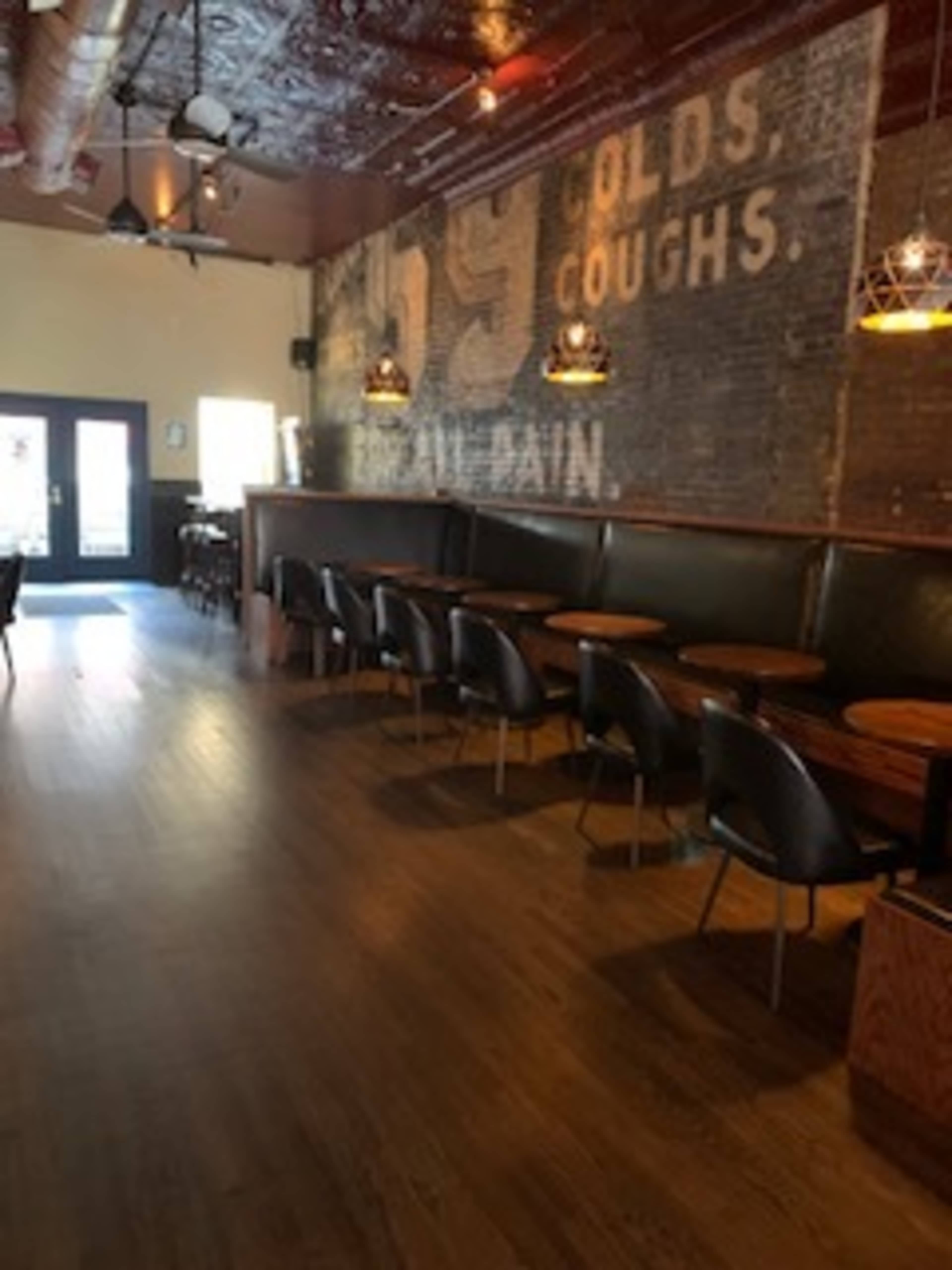 The image shows an empty café interior featuring wooden tables, black chairs, and a brick wall with faded text, illuminated by pendant lights.
