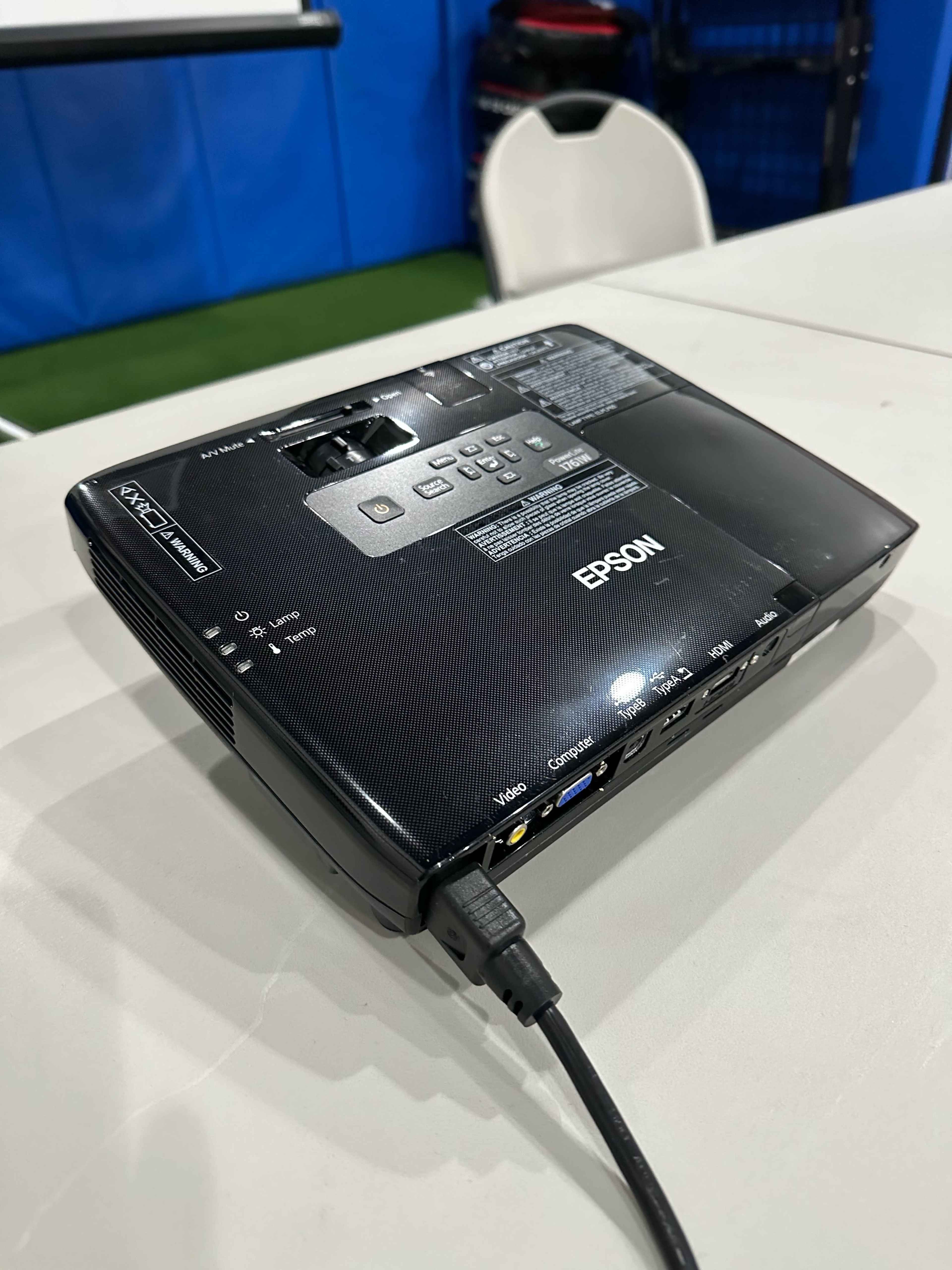 The image shows an Epson projector placed on a table, connected by a cable.