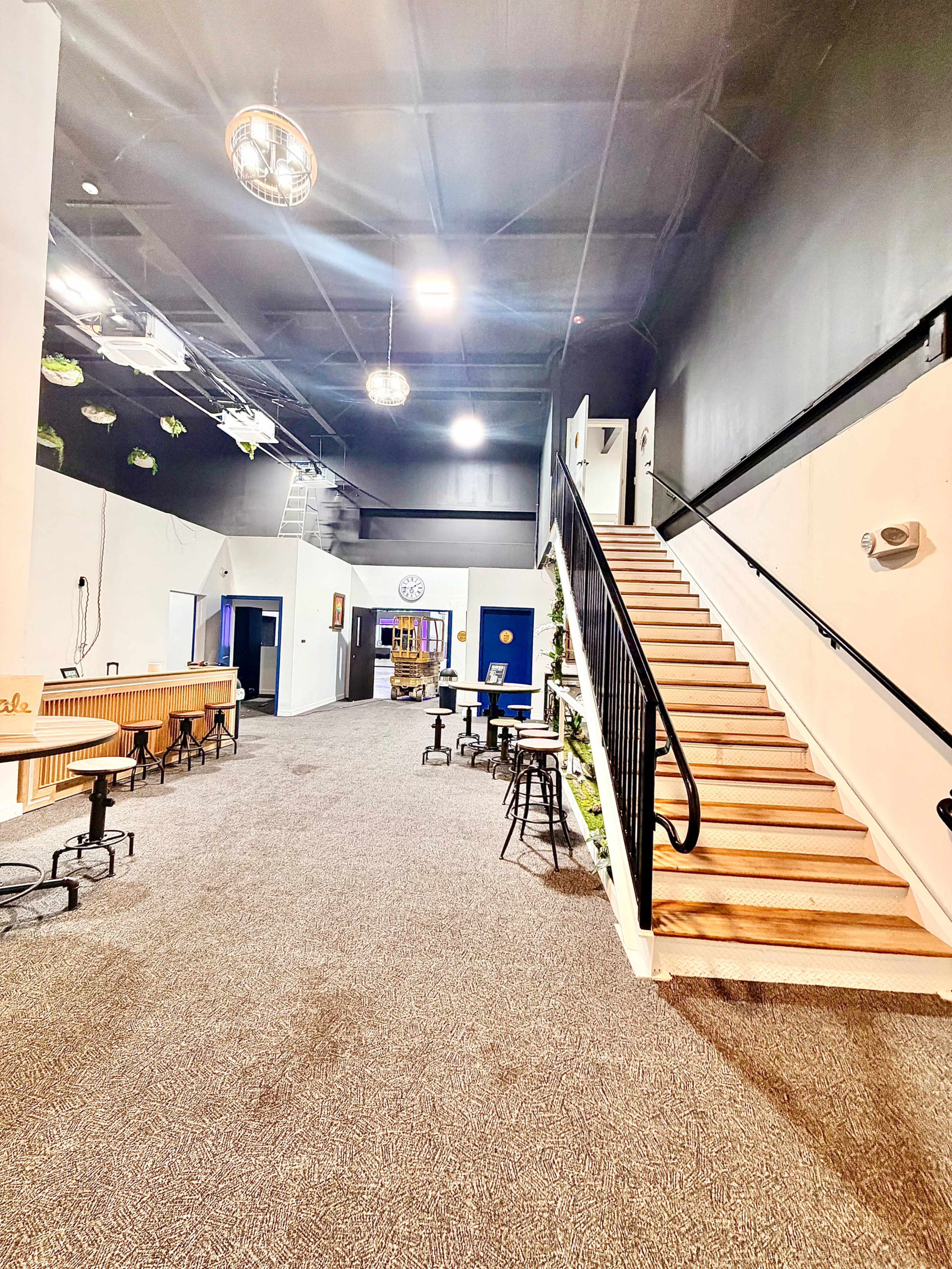 The image shows a spacious interior with a staircase on the right, a bar area on the left, and additional rooms visible in the background.