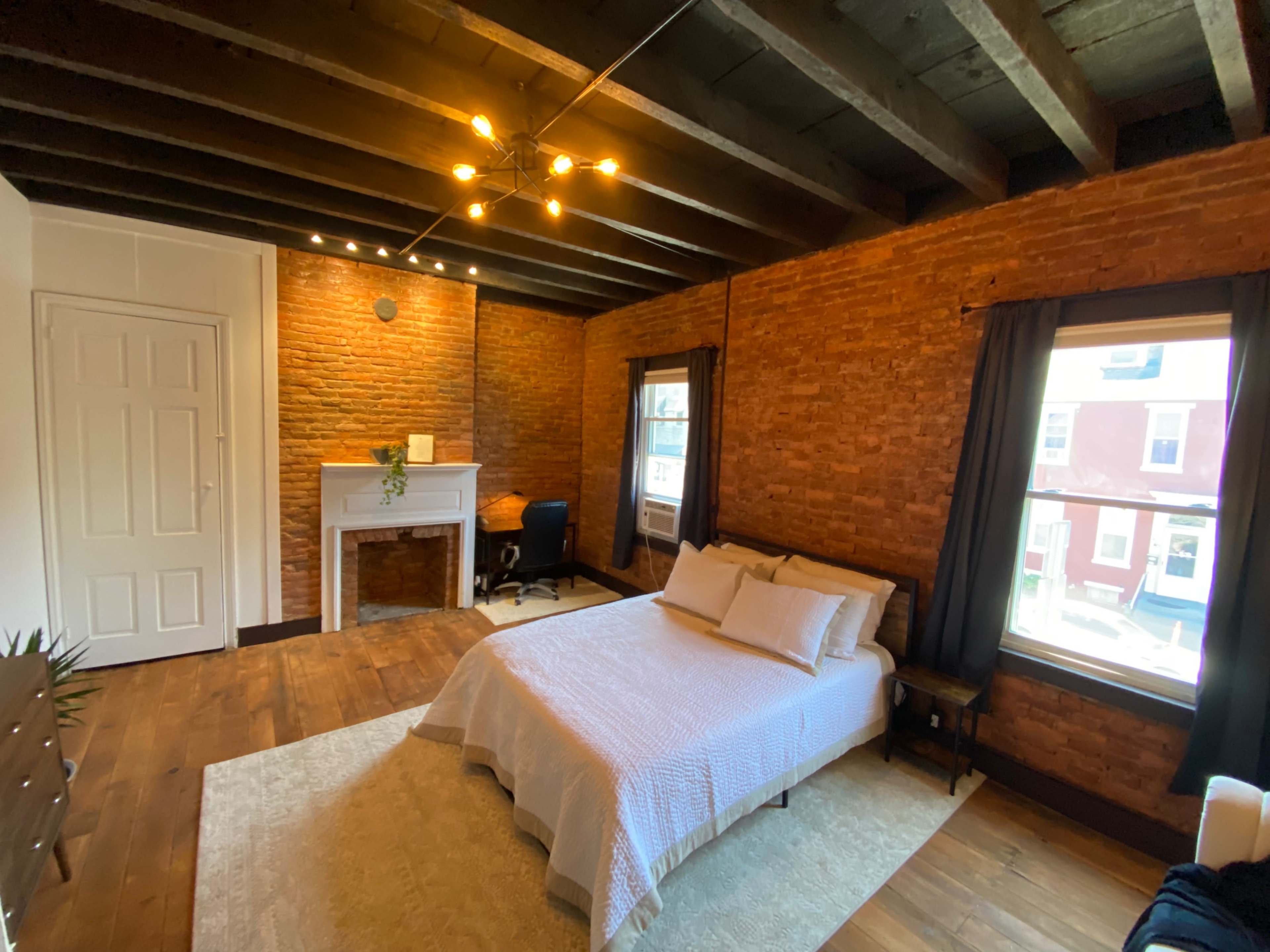 A rustic bedroom featuring exposed brick walls, wooden beams on the ceiling, and a simple bed with white bedding.