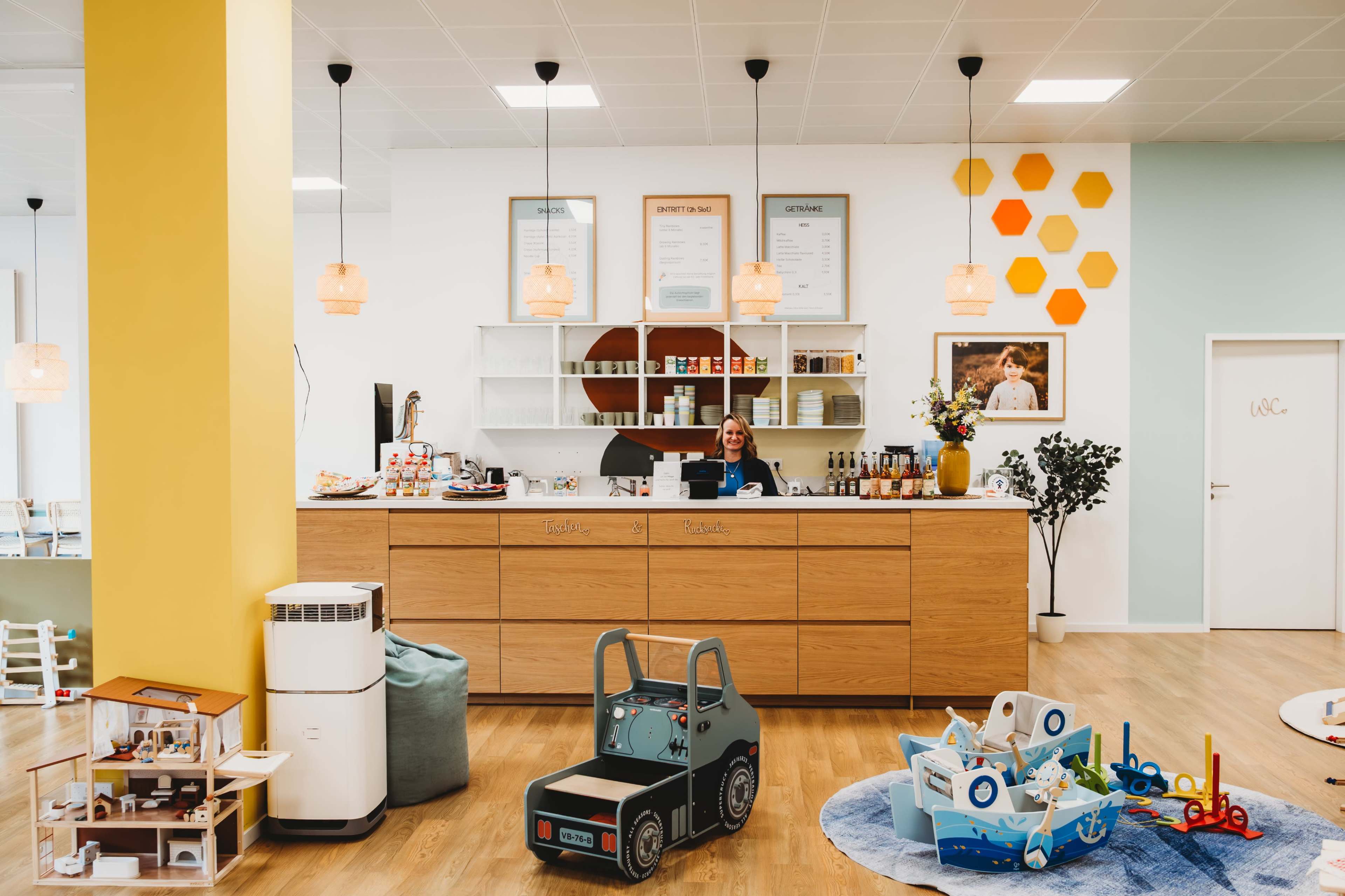A brightly lit reception area features a wooden counter with a smiling staff member, surrounded by playful children’s toys and decor.