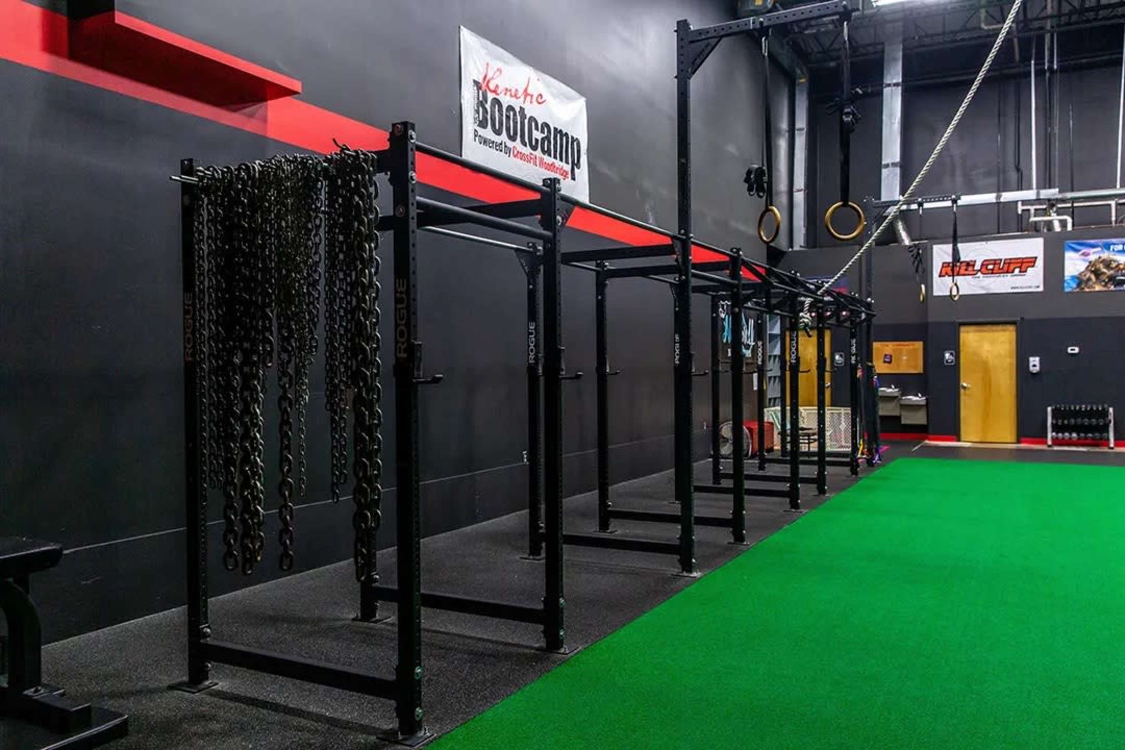 A gym interior with black workout equipment, including racks and chains, set against a green floor and a wall featuring a boot camp sign.