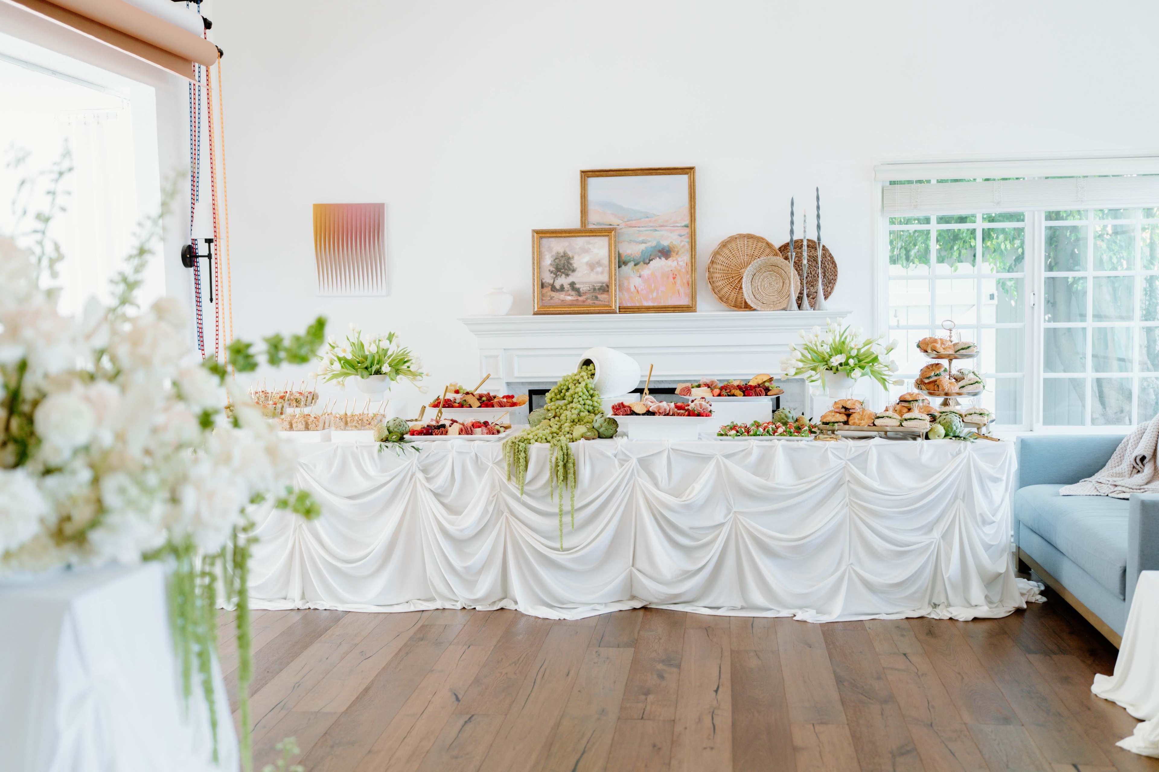 A decorated table is set with an assortment of food items, including fruits and pastries, against a backdrop of art and decorative elements.