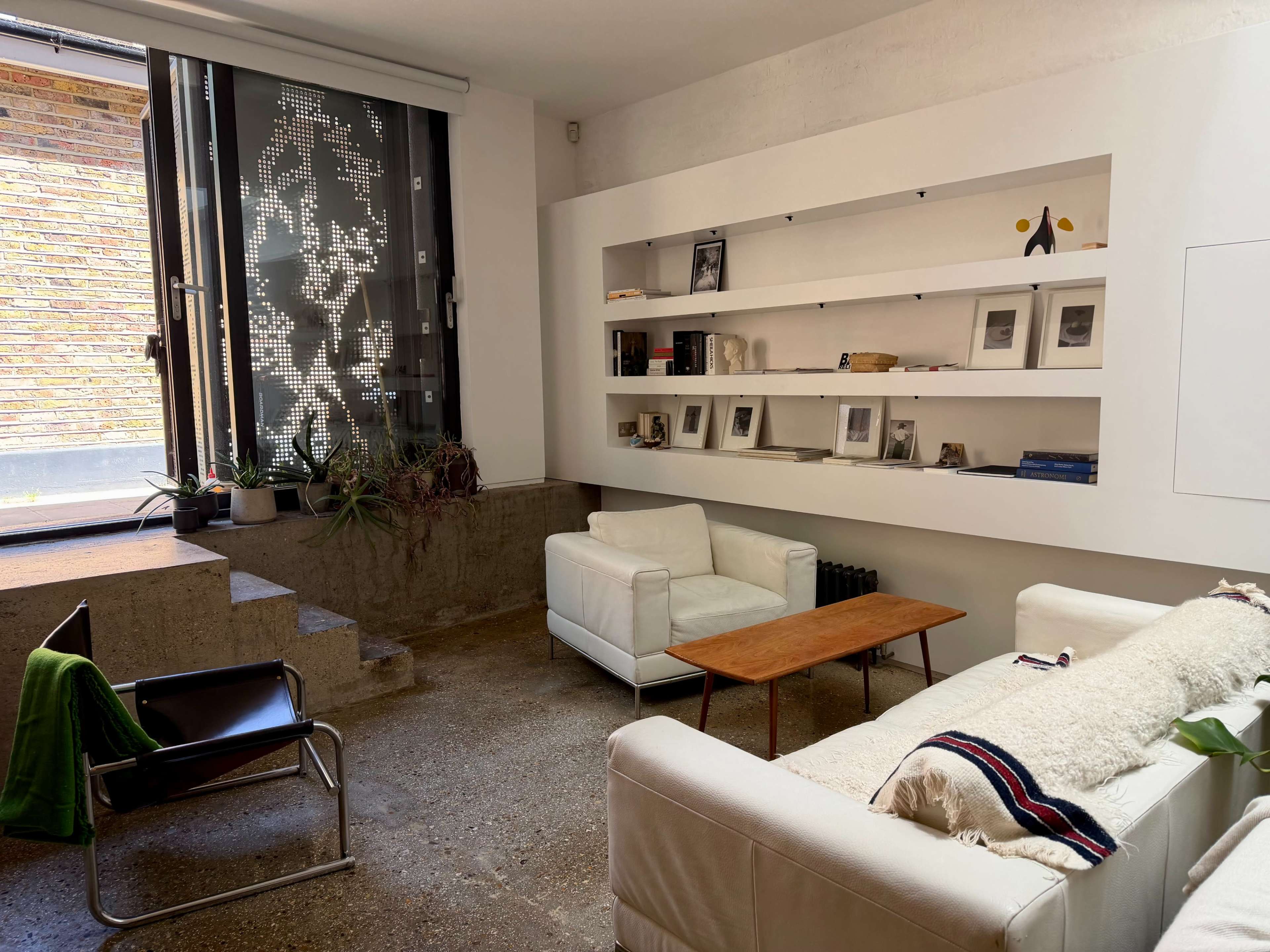 The image shows a modern living room with a white sofa, a wooden coffee table, and shelves displaying various items.