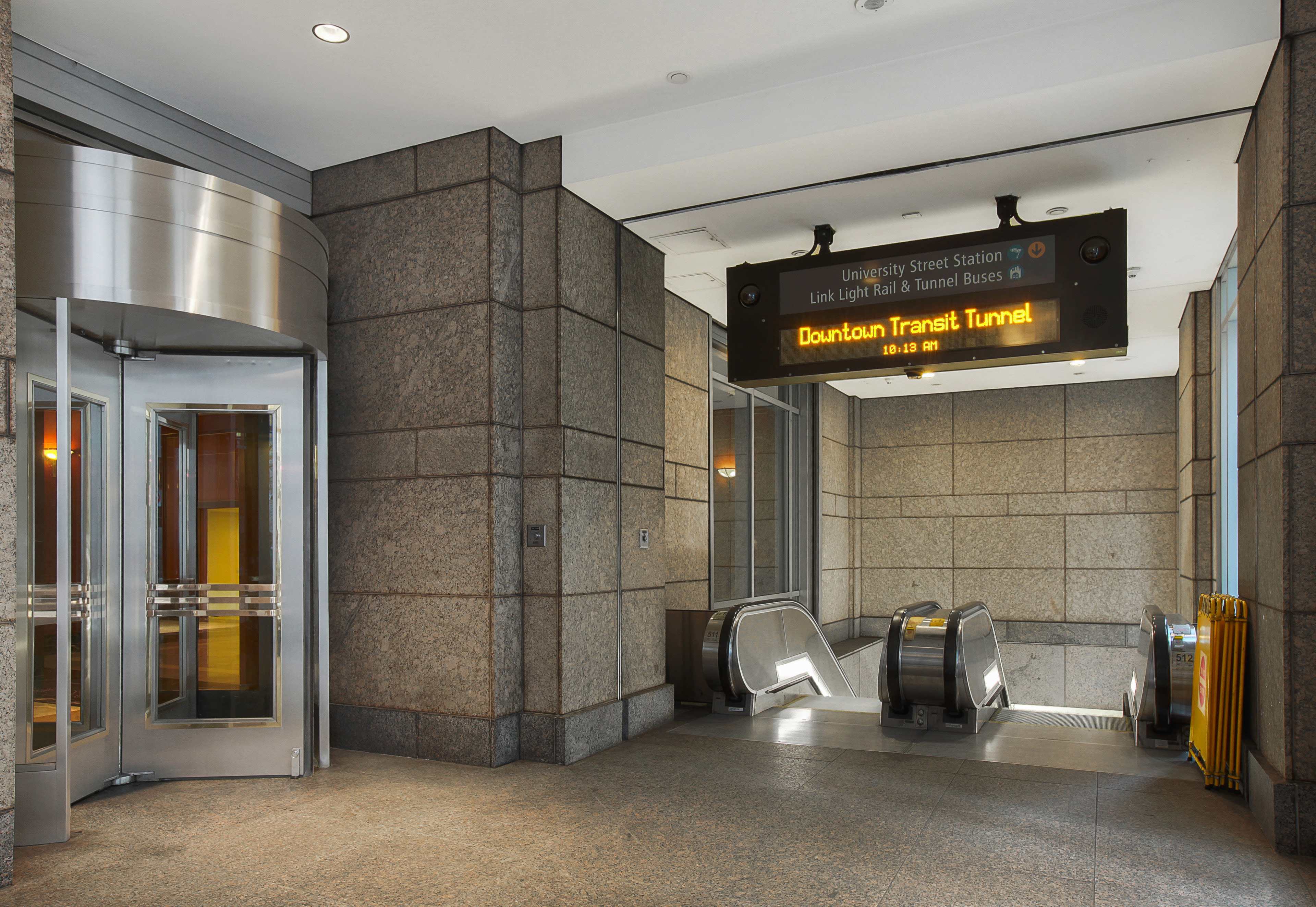 A transit station entrance with an electronic display board and an escalator leading to the platform area.