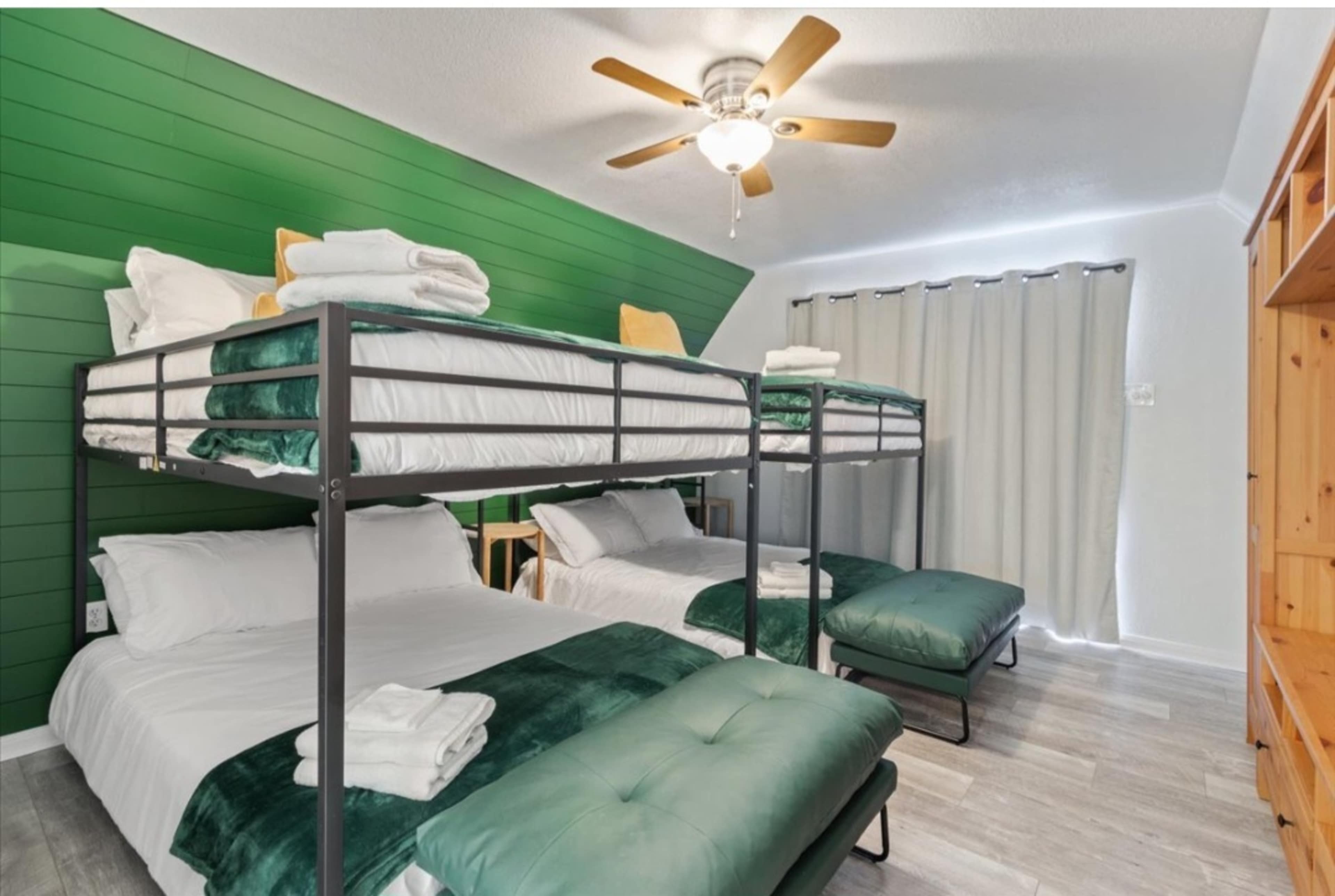 A modern bedroom with two sets of bunk beds and two double beds, all featuring green accents and a ceiling fan.