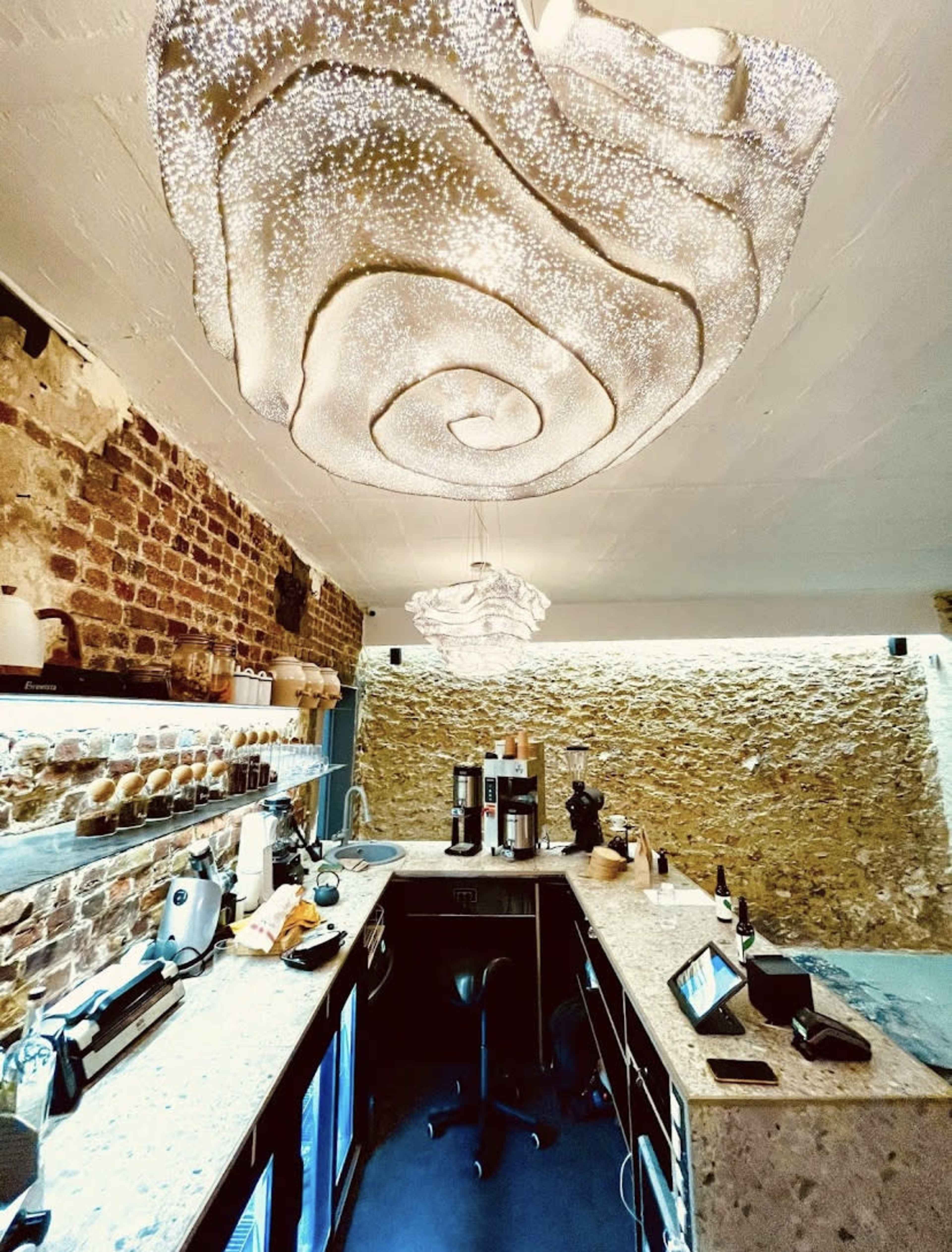 A modern café interior with a sleek bar area featuring pendant lights and stone walls.