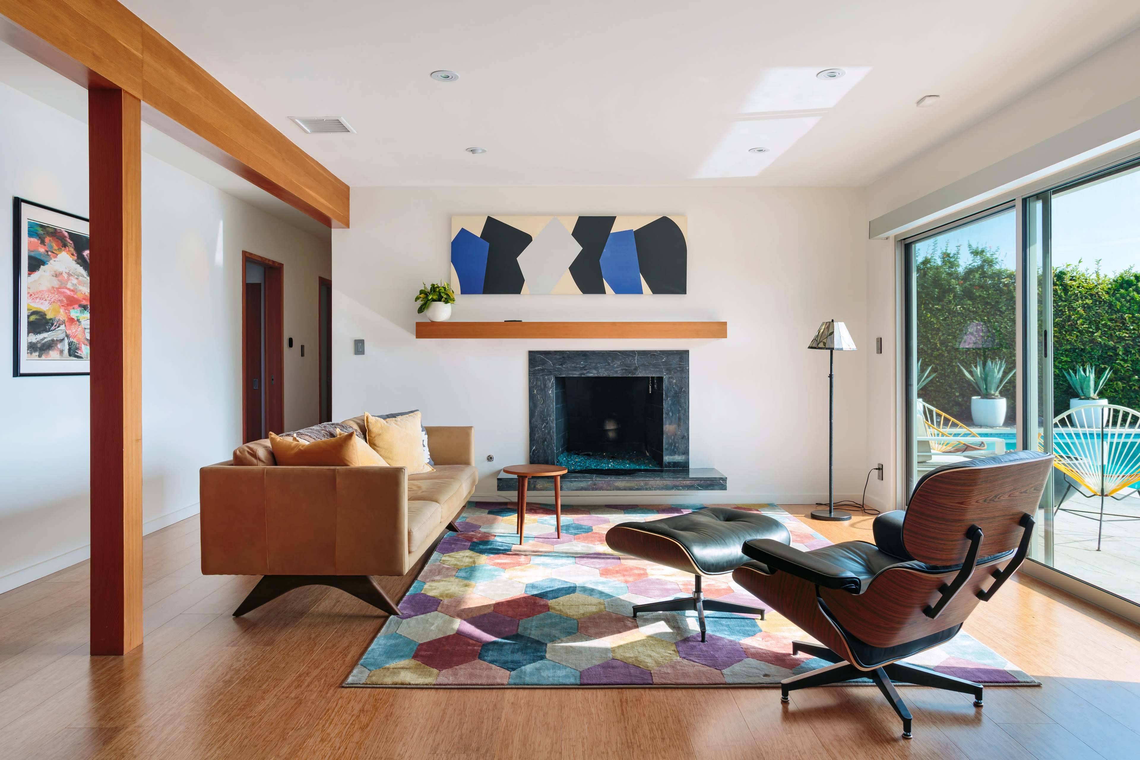 A modern living room featuring a brown sofa, a geometric-patterned rug, a black stone fireplace, and large glass doors leading to an outdoor patio.