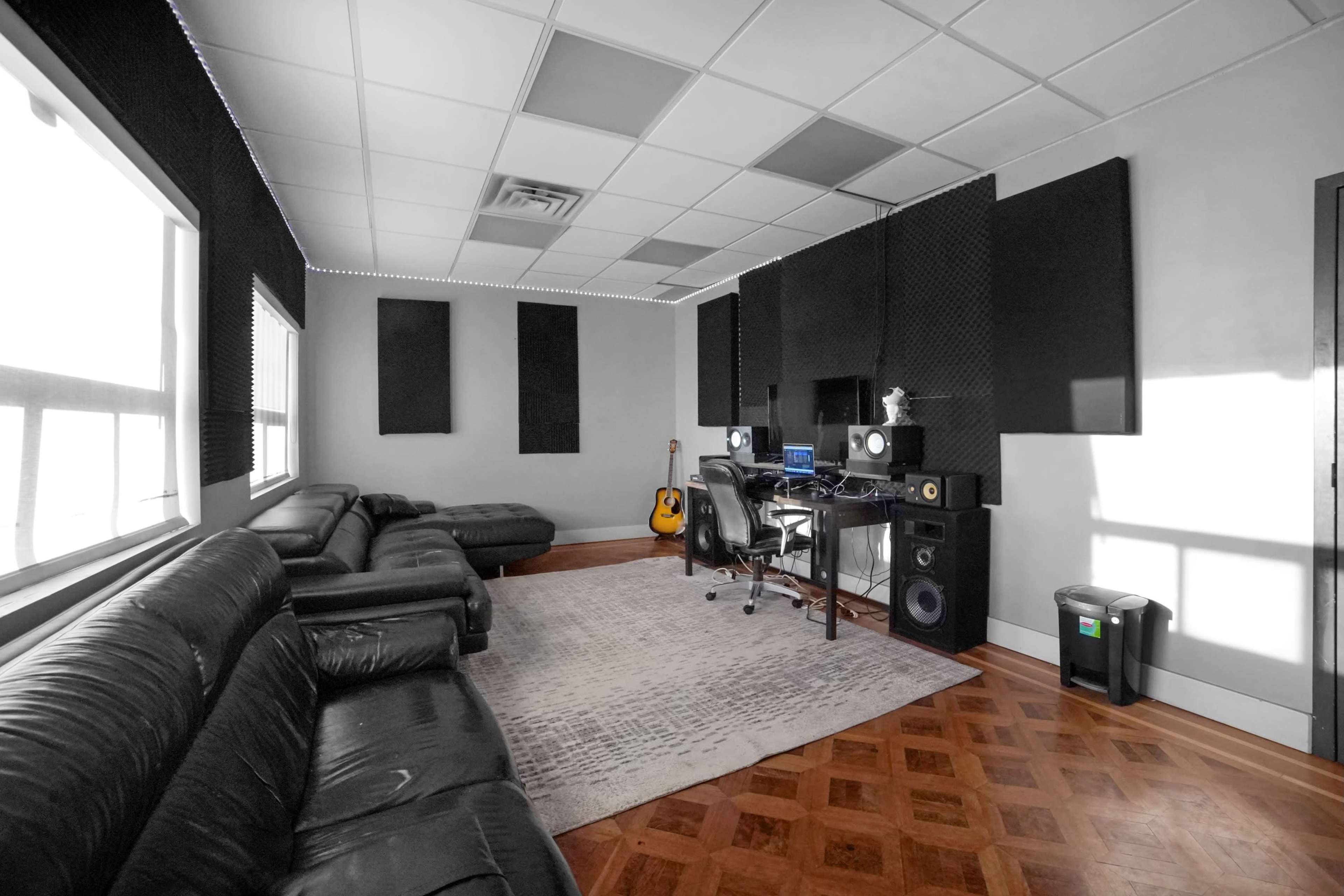 A music studio with black leather couches, a workstation equipped with monitors and speakers, and acoustic panels on the walls.