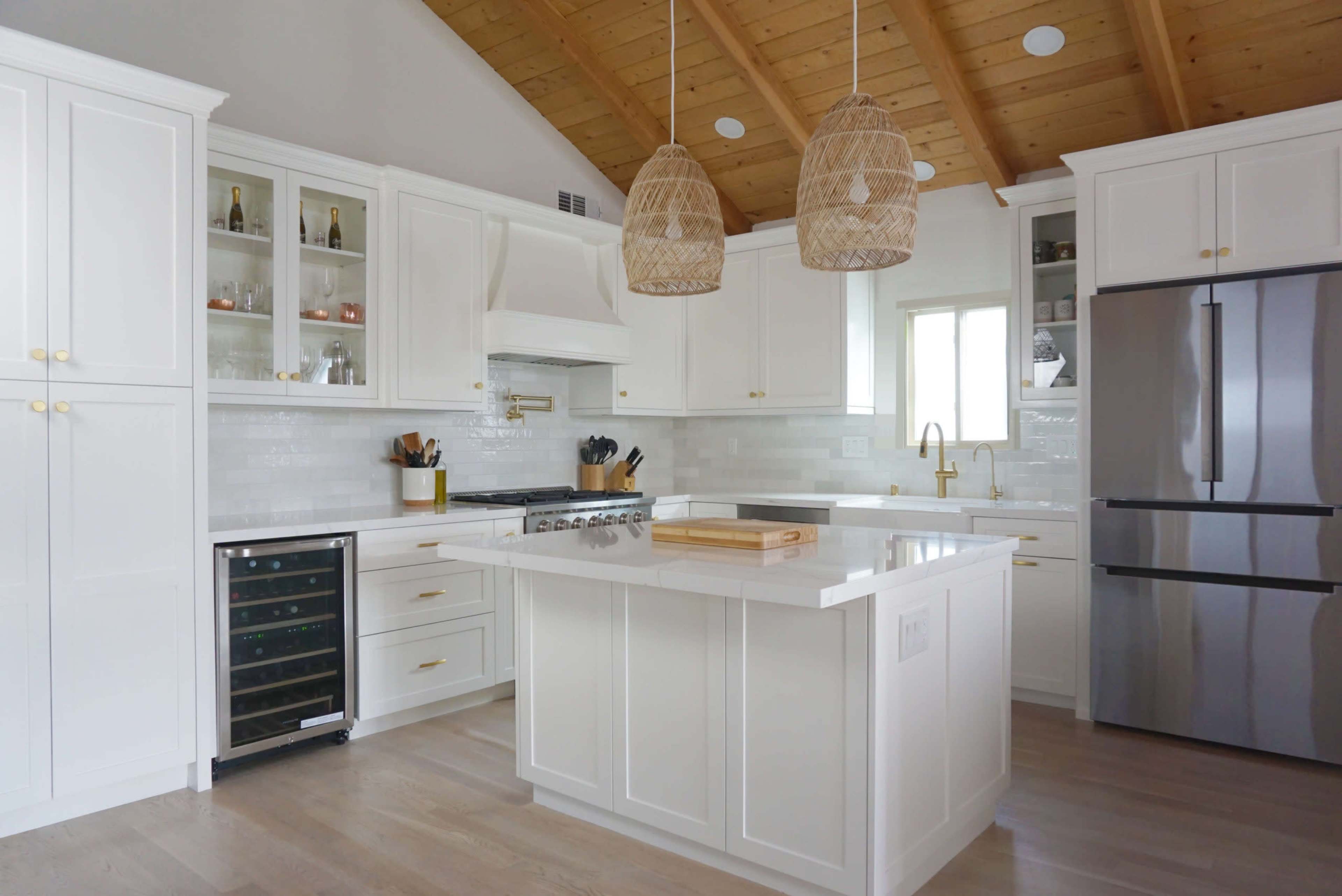 The kitchen features a central island with a white countertop, wooden ceilings, and pendant lights, along with modern appliances and cabinetry.