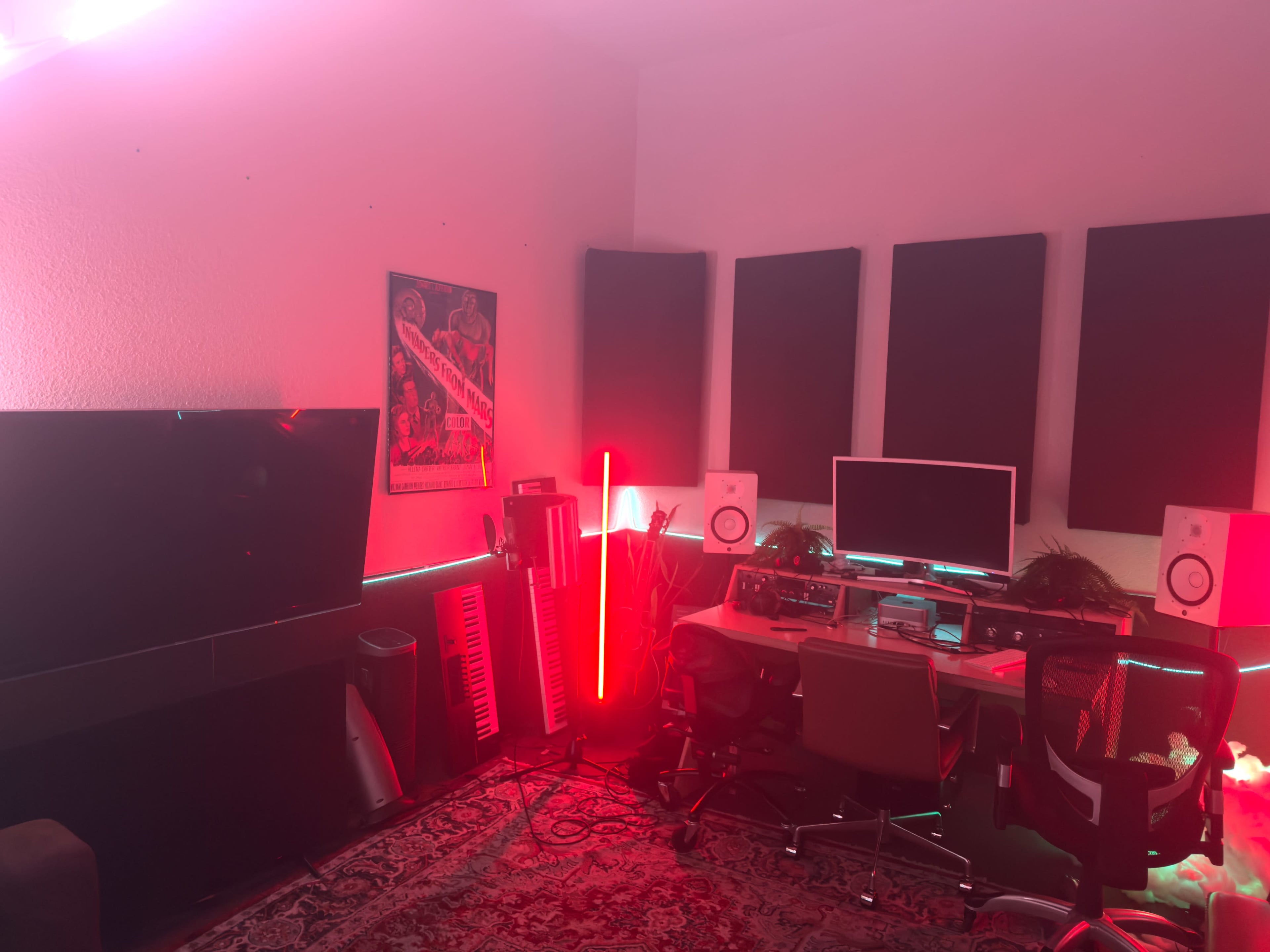 The image shows a modern recording studio featuring a computer workstation, music equipment, and colorful lighting against a wall with acoustic panels.