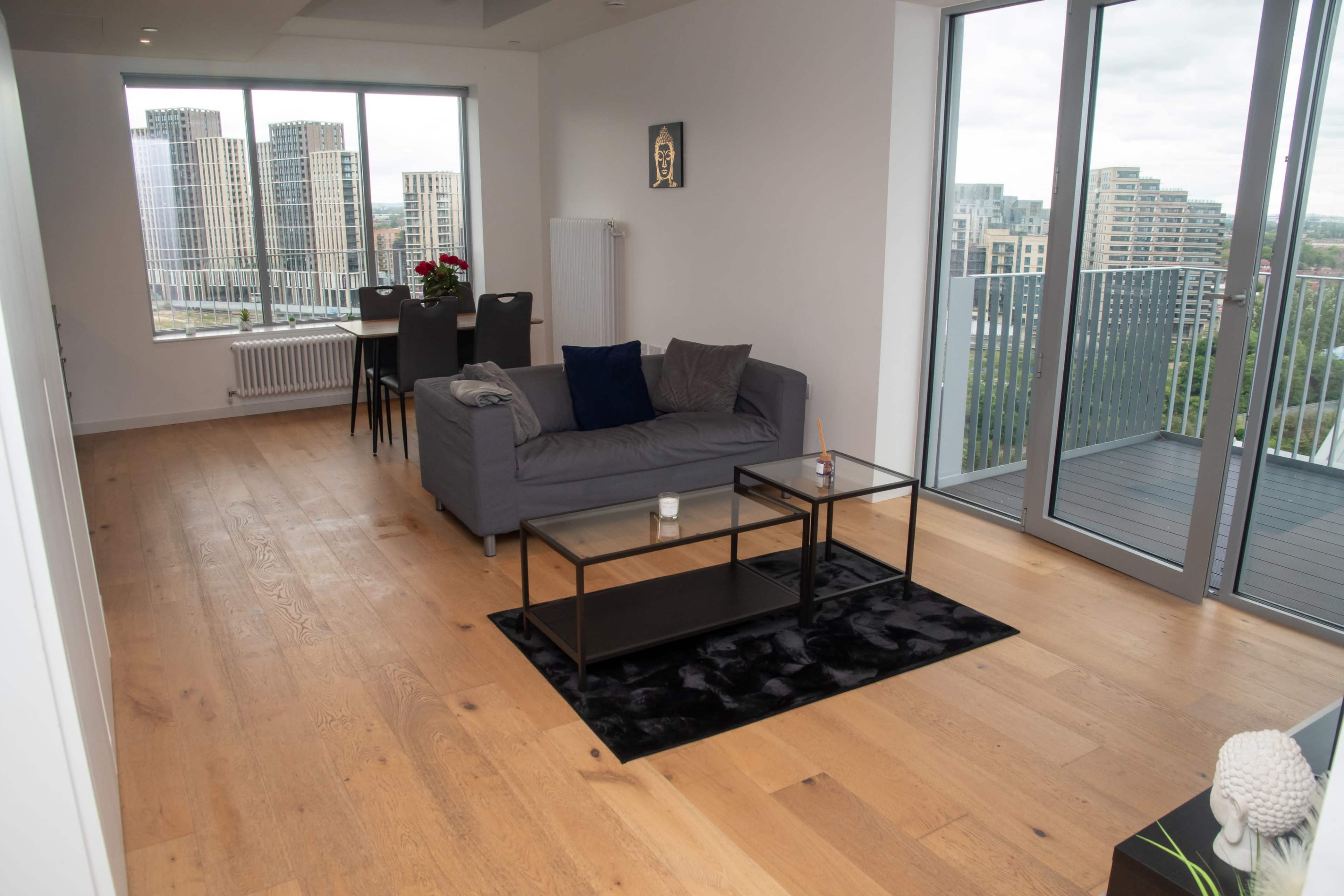 A modern living room with a gray sofa, a glass coffee table on a black rug, and large windows overlooking a cityscape.