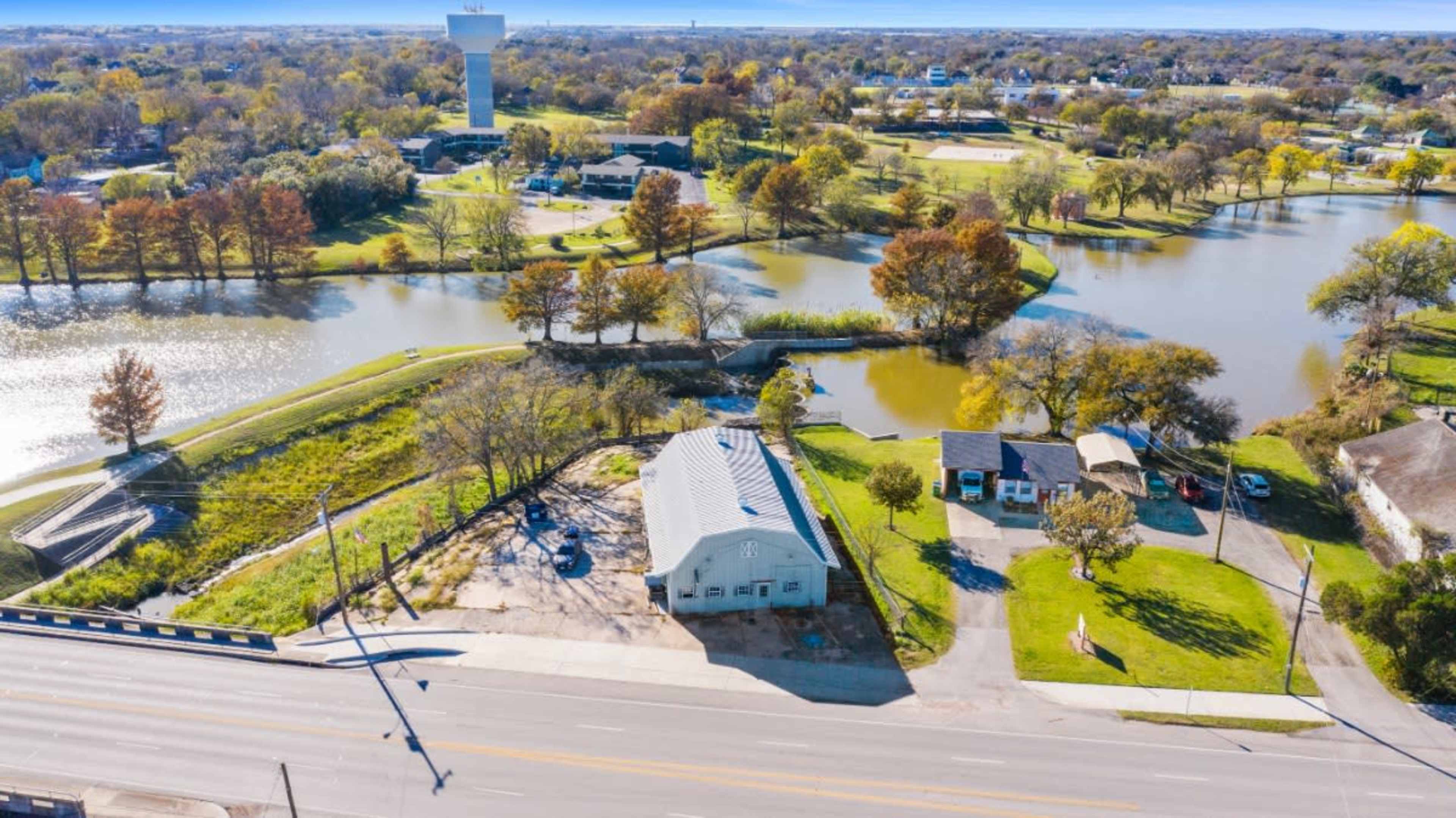 The image shows an aerial view of a landscape featuring a house near a water body, with several trees and a park-like area in the background.
