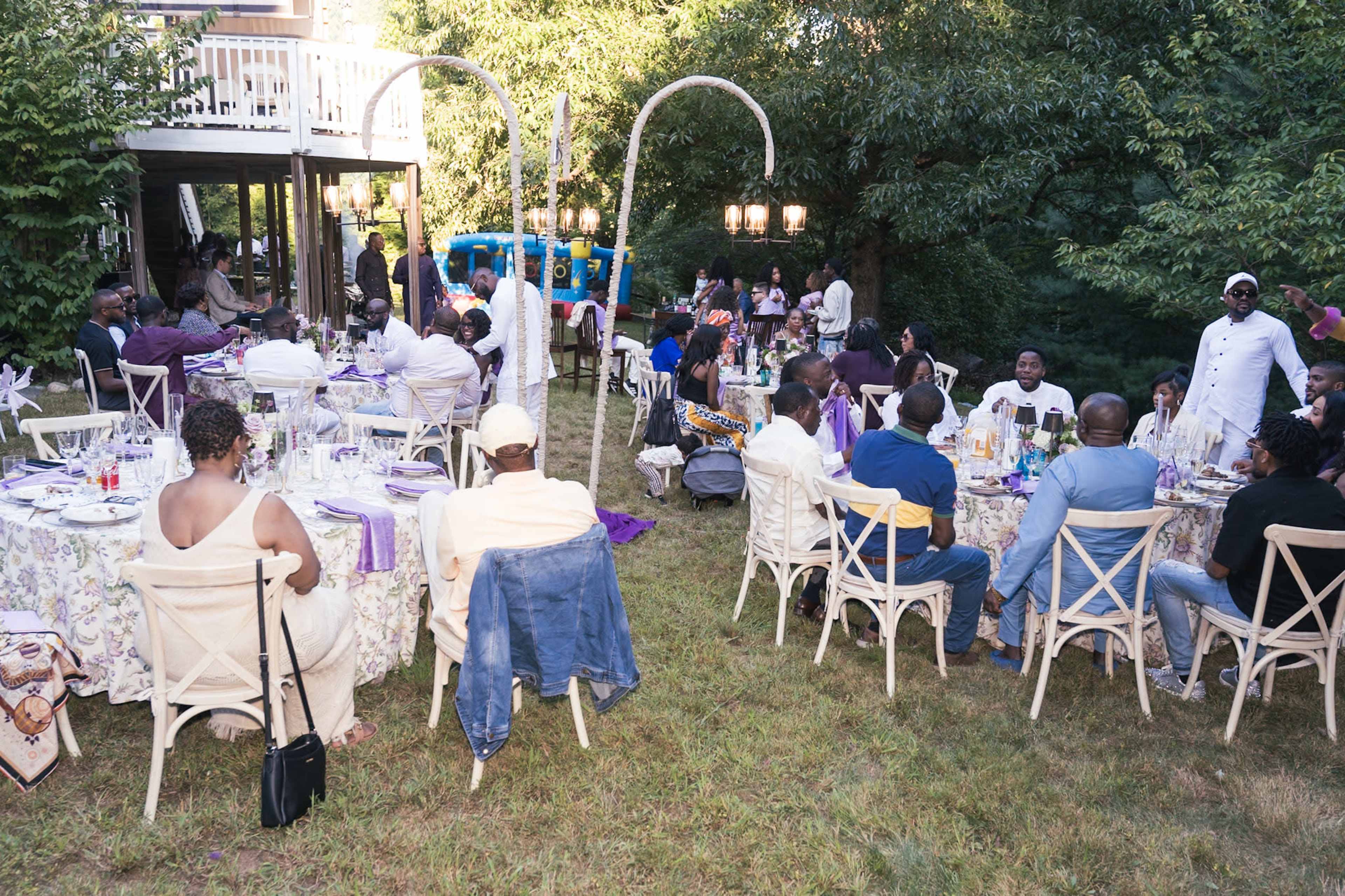 A group of people is seated at elegantly decorated tables in a backyard, engaged in conversation during a social gathering.
