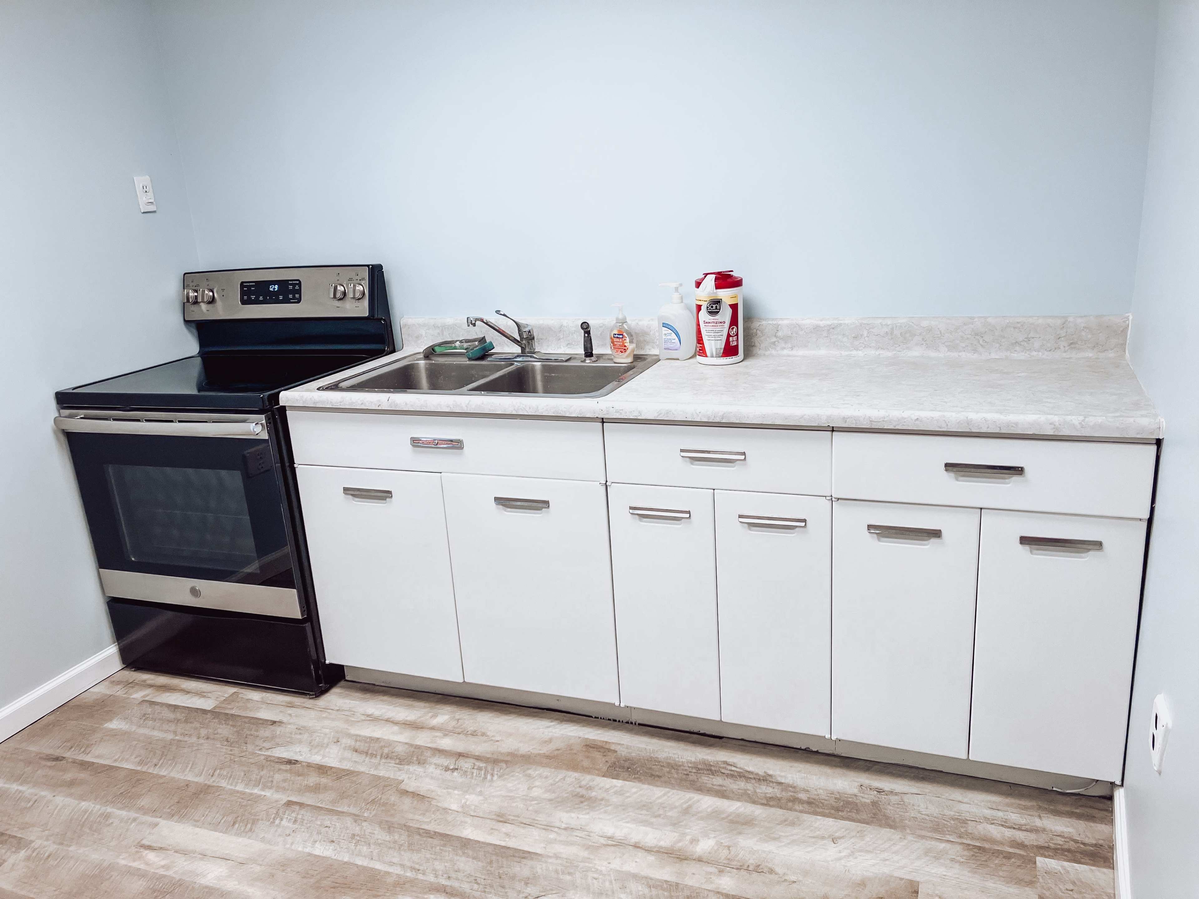 A kitchen with a stainless steel stove, a double sink, and white cabinets arranged along a light-colored wall.