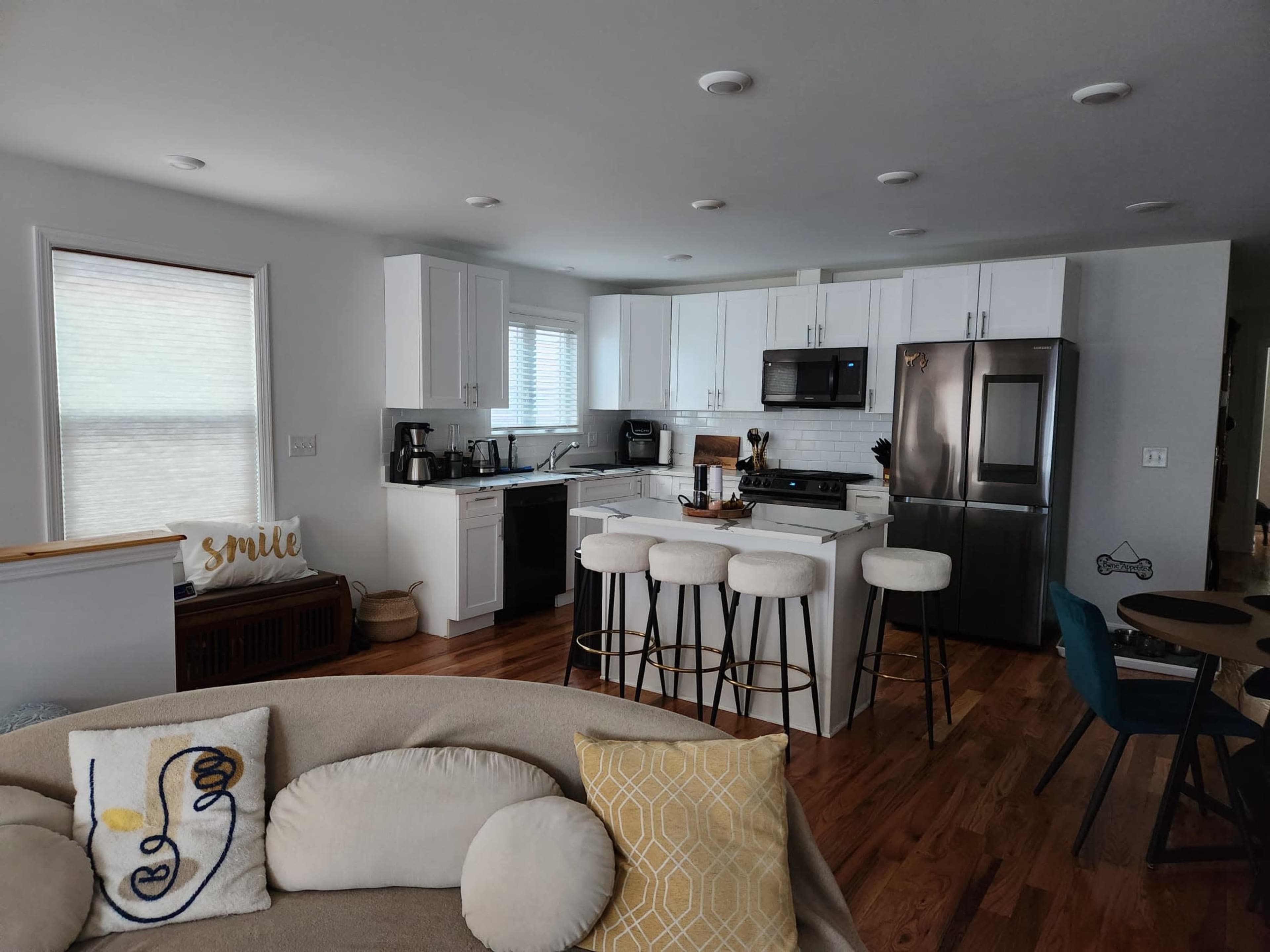 A modern kitchen with white cabinetry, stainless steel appliances, and a dining area featuring bar stools and a round table.