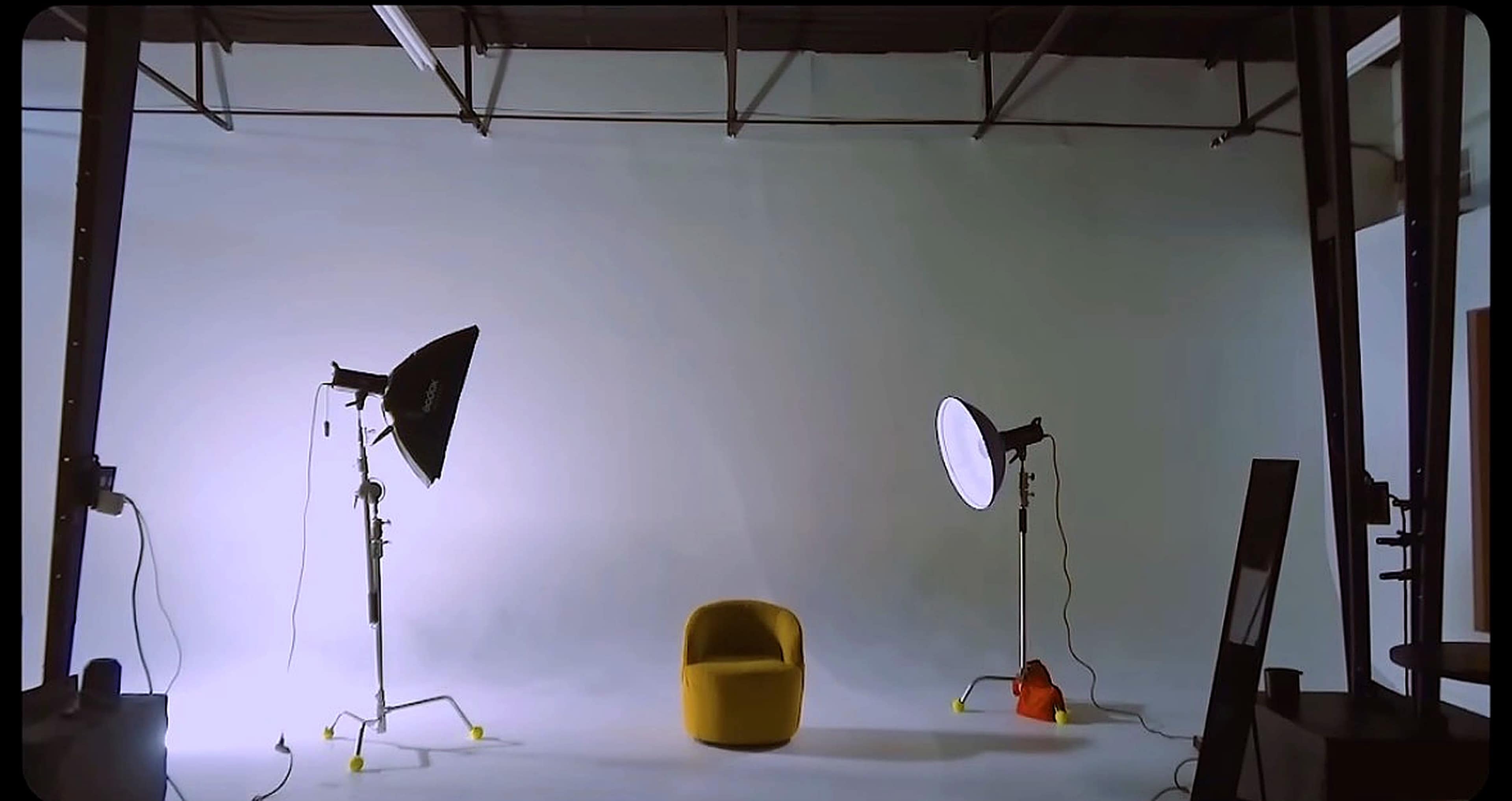 The image shows a photography studio with two light stands positioned on either side of a yellow chair against a plain background.