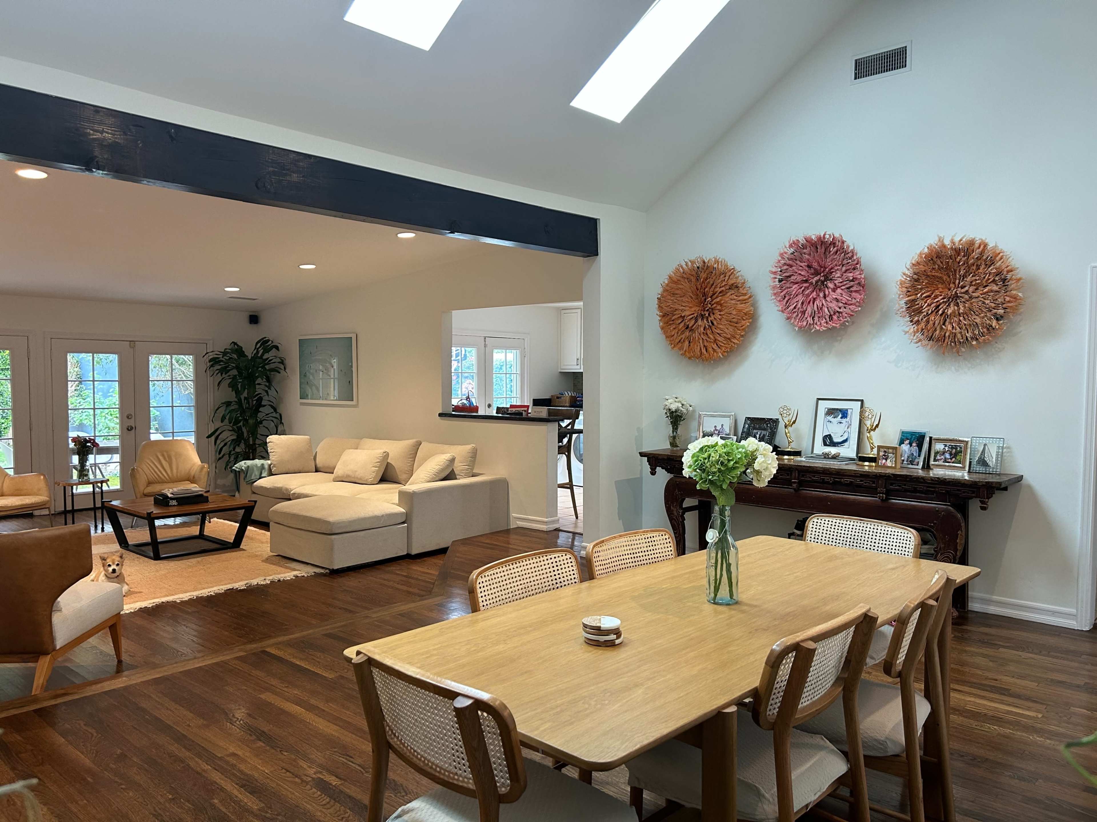 A light-filled open-concept living and dining area features a large sectional sofa, a wooden dining table, and colorful wall decorations.