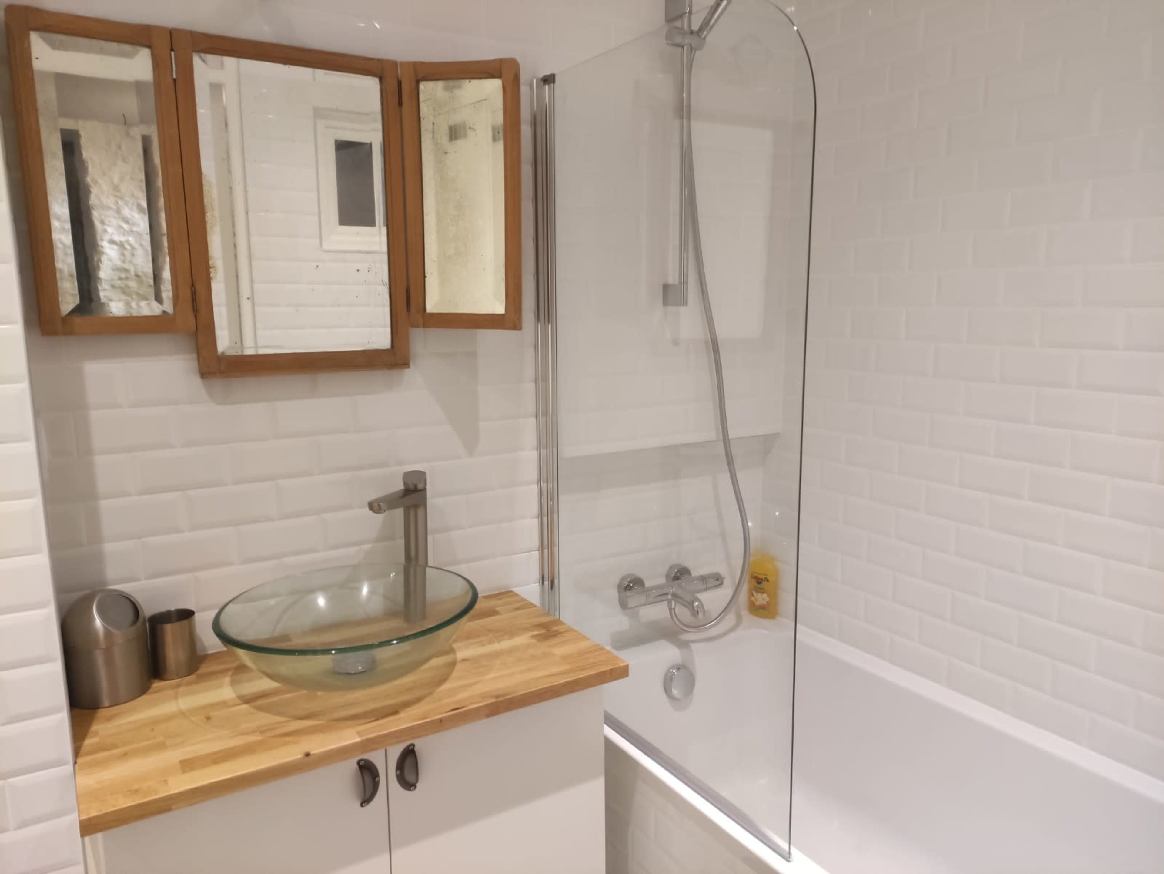 A modern bathroom with a glass shower enclosure, a wooden countertop, a vessel sink, and a mirror above the sink.