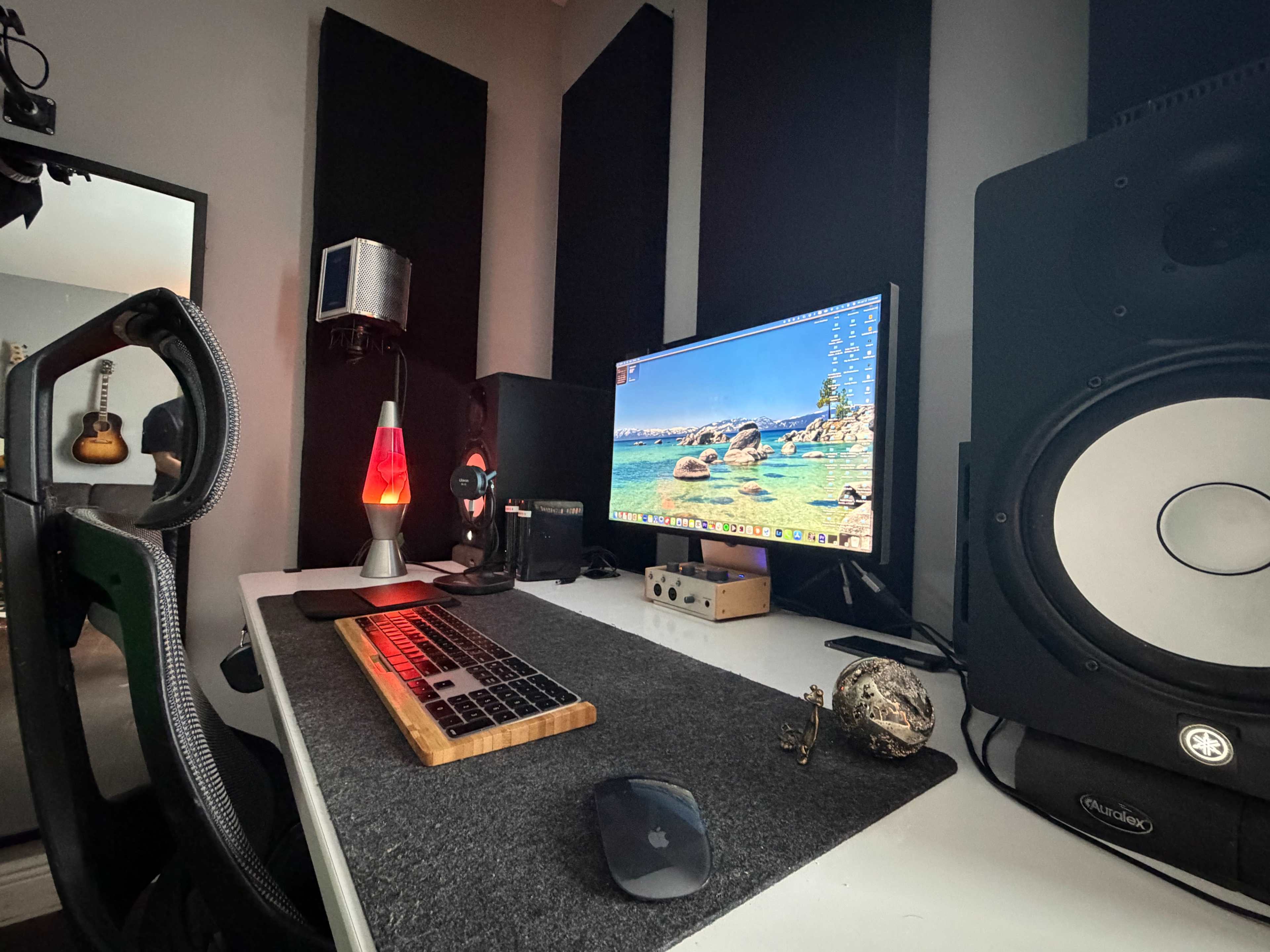 The image shows a workspace featuring a computer monitor, keyboard, mouse, audio speakers, and a lava lamp, with soundproof panels on the walls.