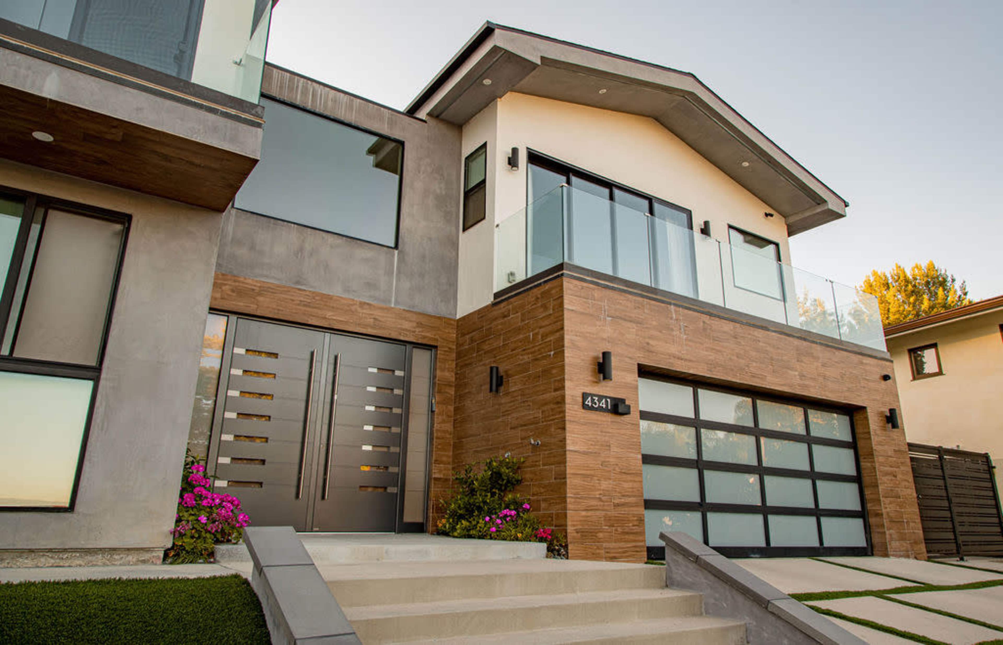 A modern two-story house with a combination of concrete and wood finishes, featuring large windows and a spacious front entrance with landscaped steps.