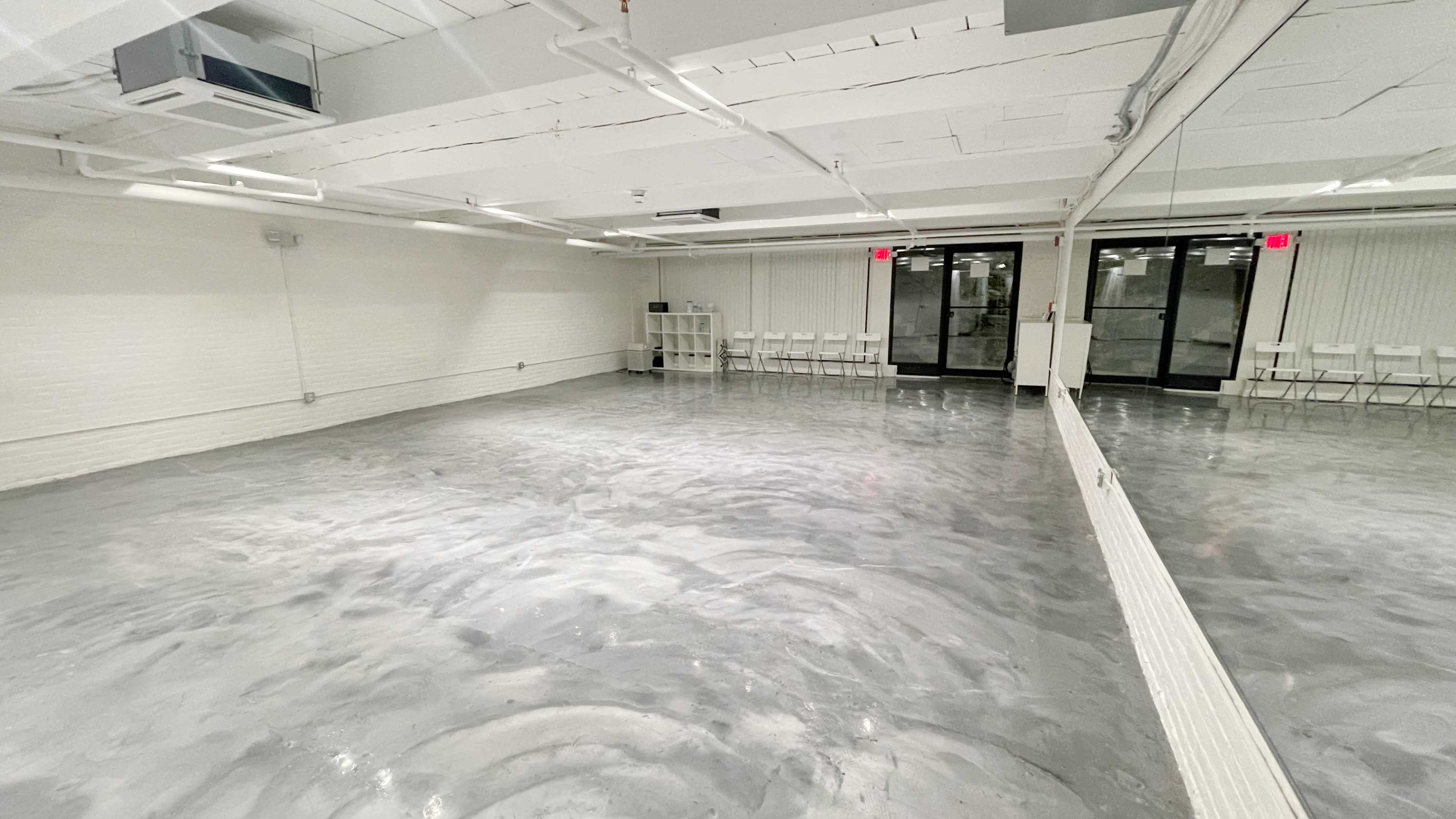 A spacious, empty studio with a polished gray concrete floor and large windows allowing natural light.