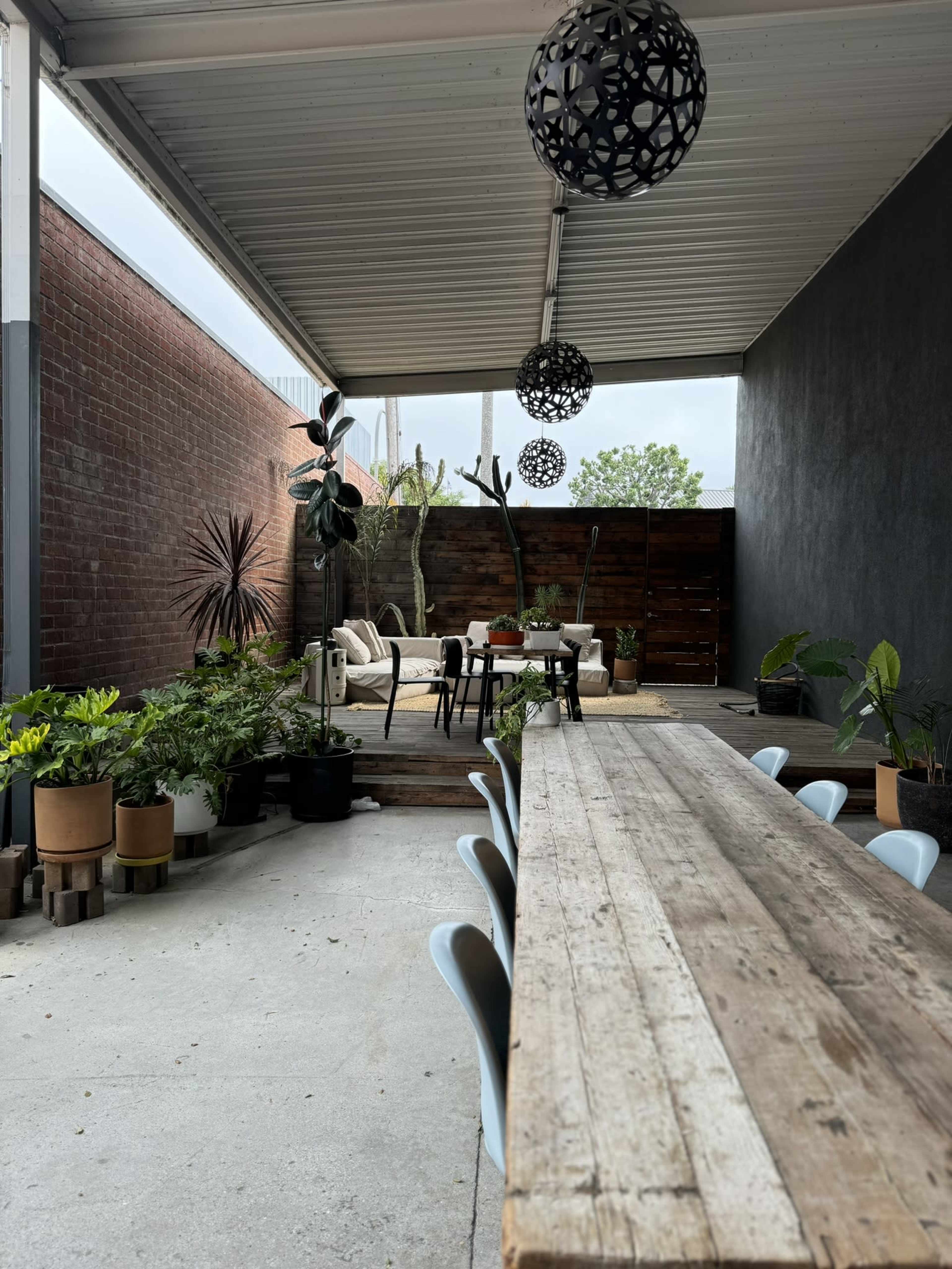 A covered outdoor space featuring a wooden dining table, various potted plants, and seating arrangements.