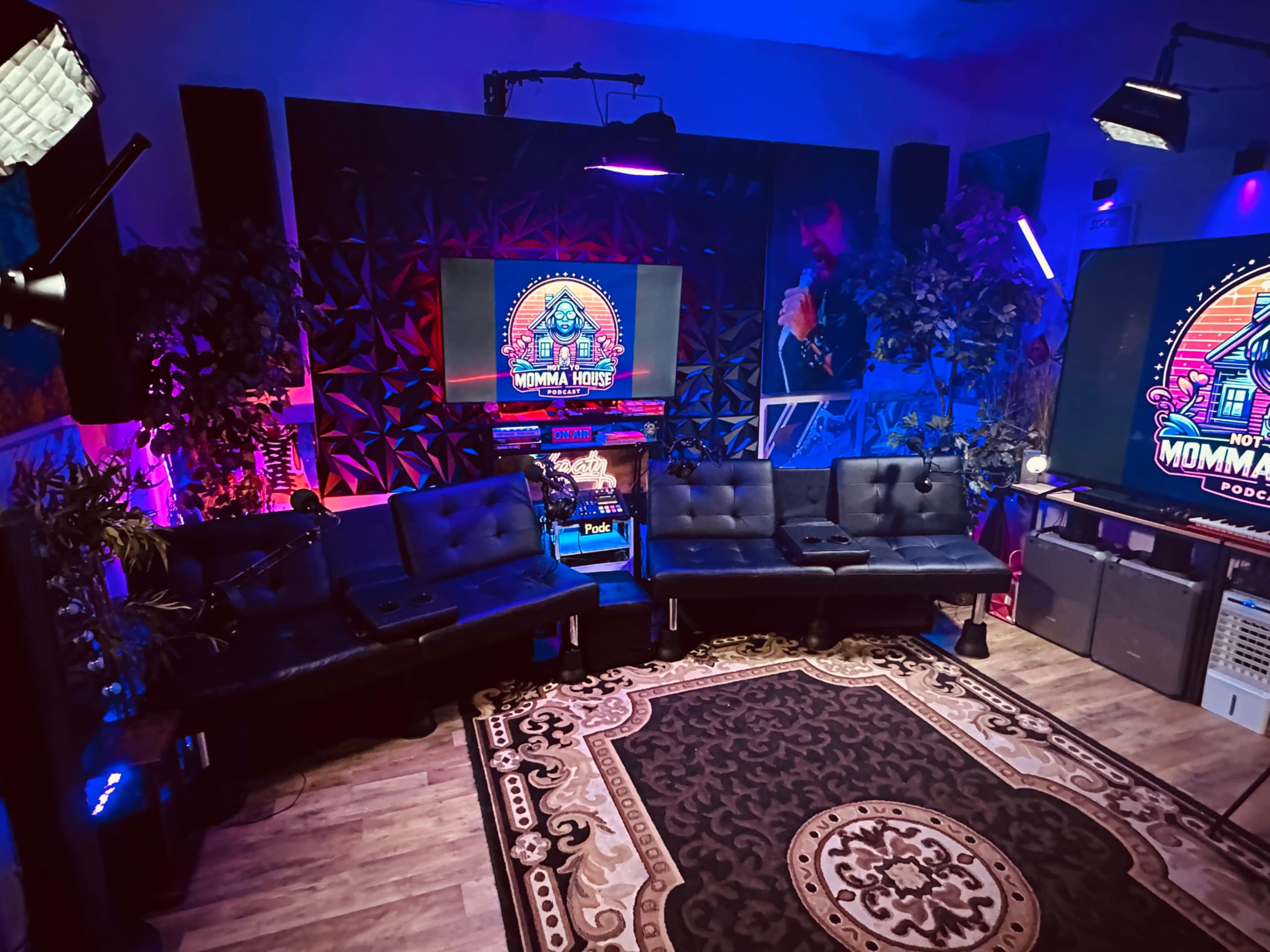 The image shows a modern podcast studio featuring black couches, colorful lighting, large screens displaying a logo, and decorative plants.