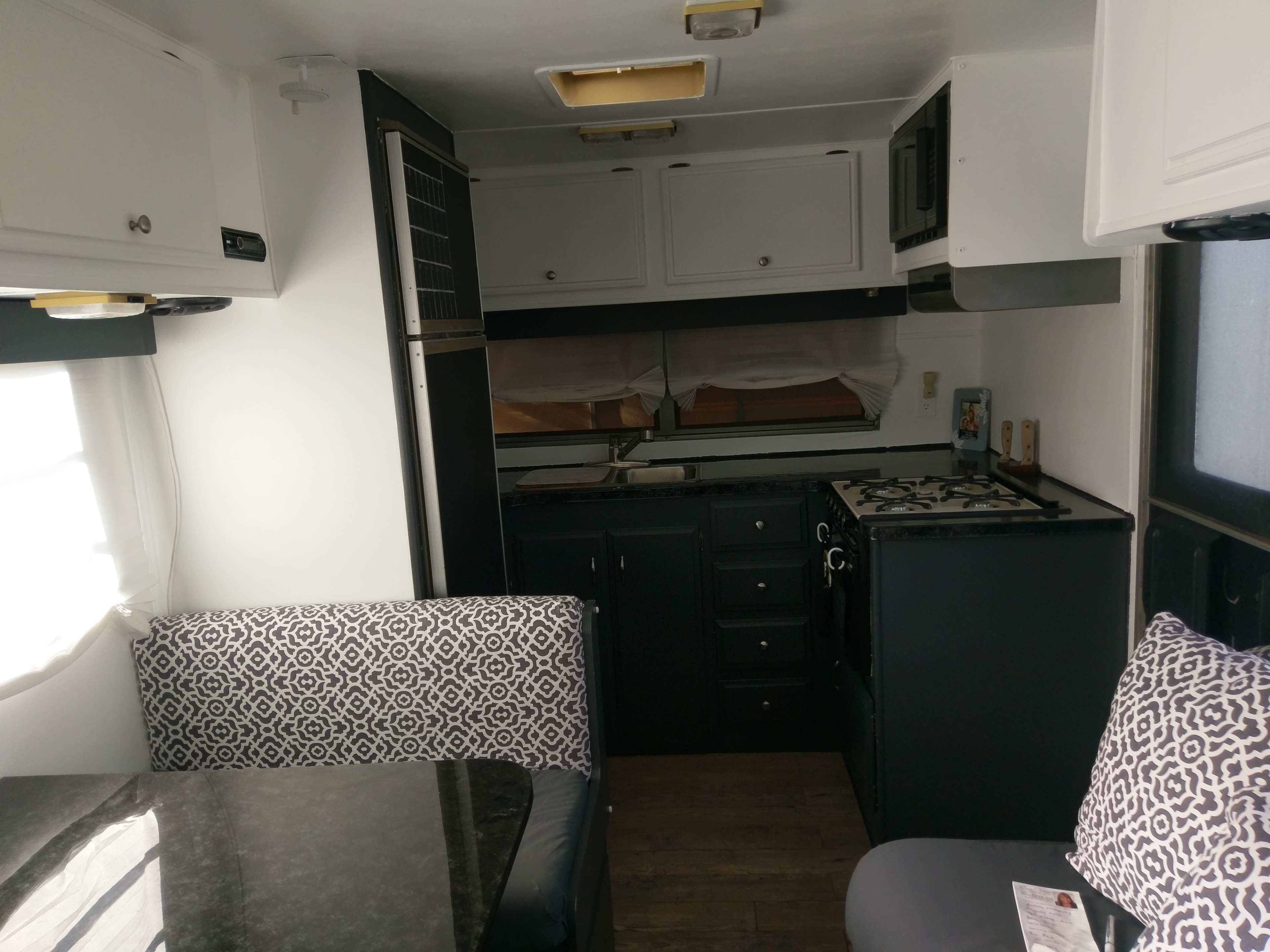 The interior of a camper, featuring a kitchen area with cabinets, a stove, and a dining nook with patterned cushions.