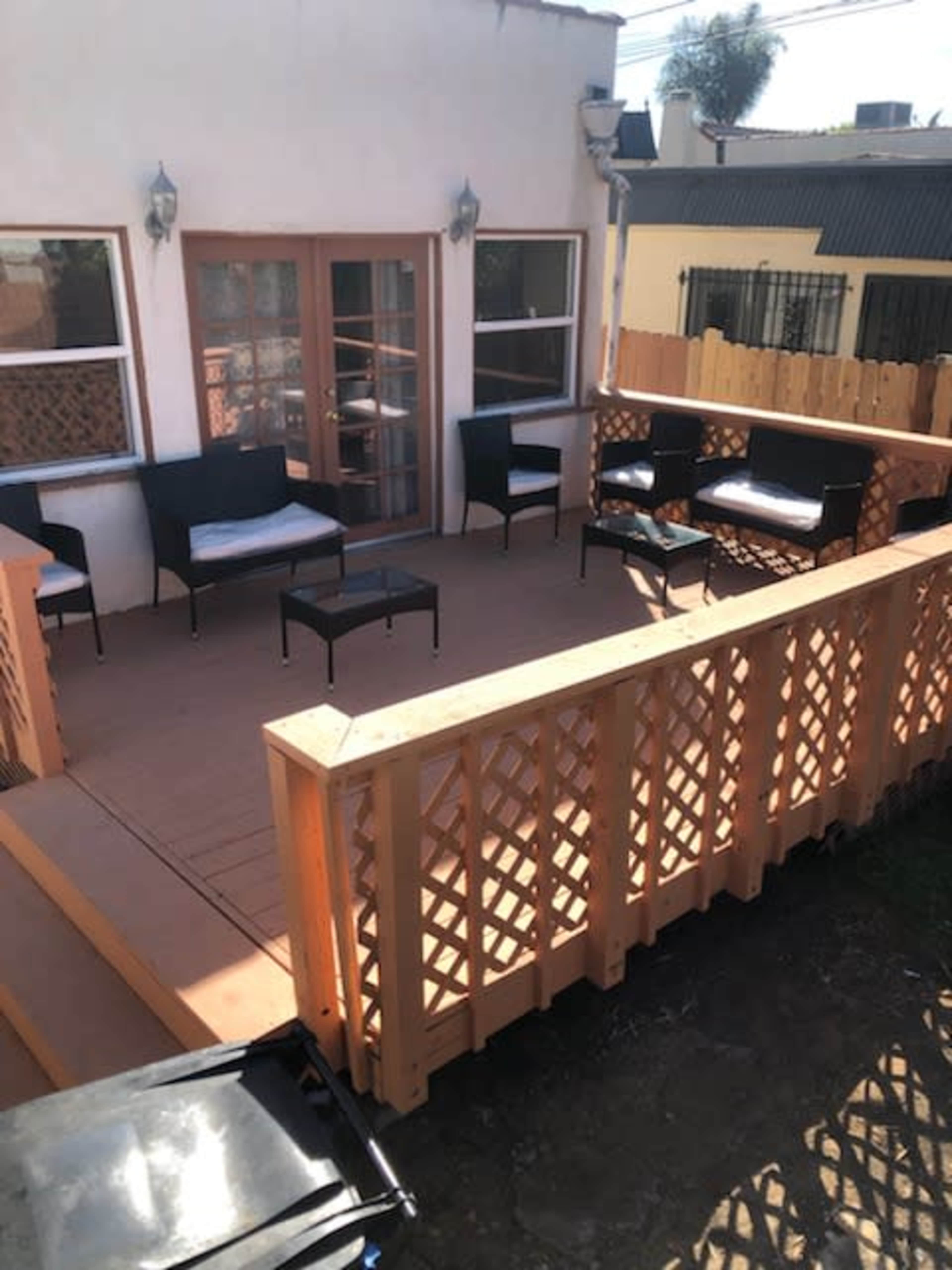 The image shows a patio area with several black wicker chairs and a small table, surrounded by a wooden railing and adjacent to a building.