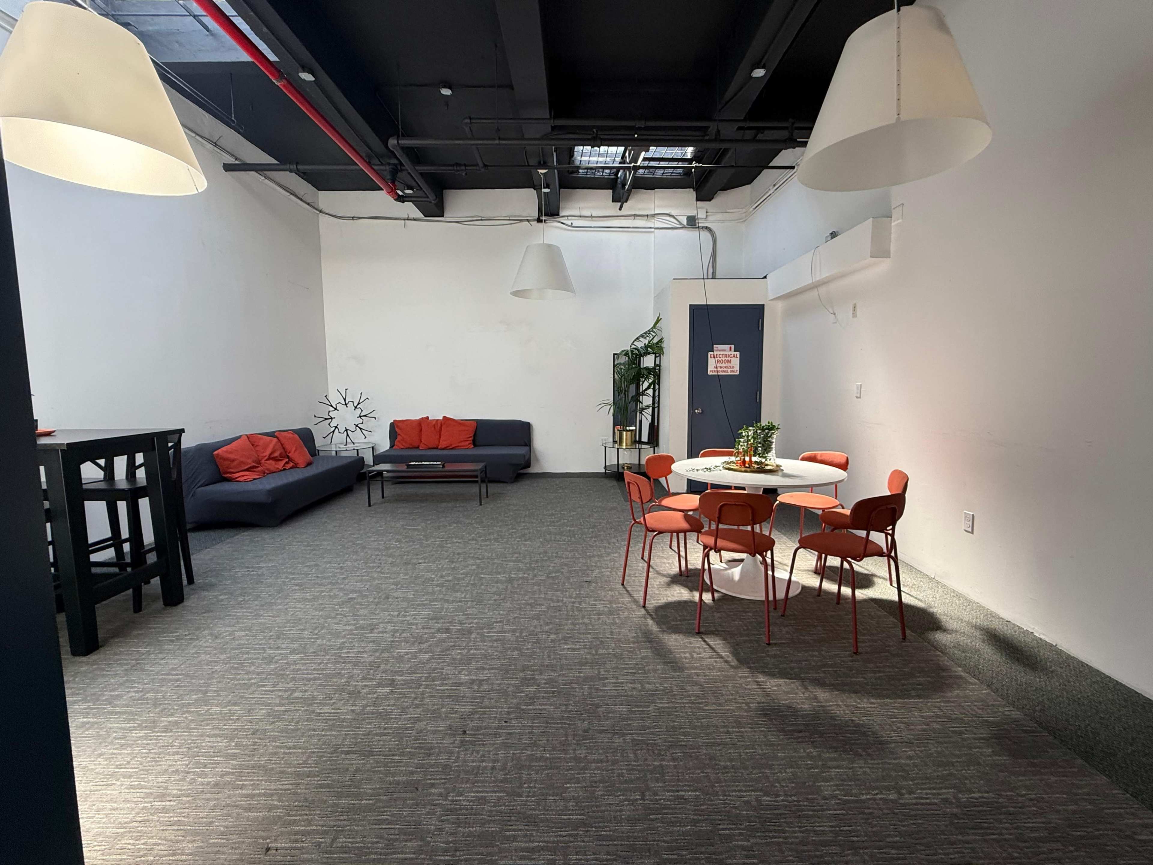 The image shows a spacious, well-lit room furnished with a sofa, a dining table surrounded by chairs, and a few decorative elements.