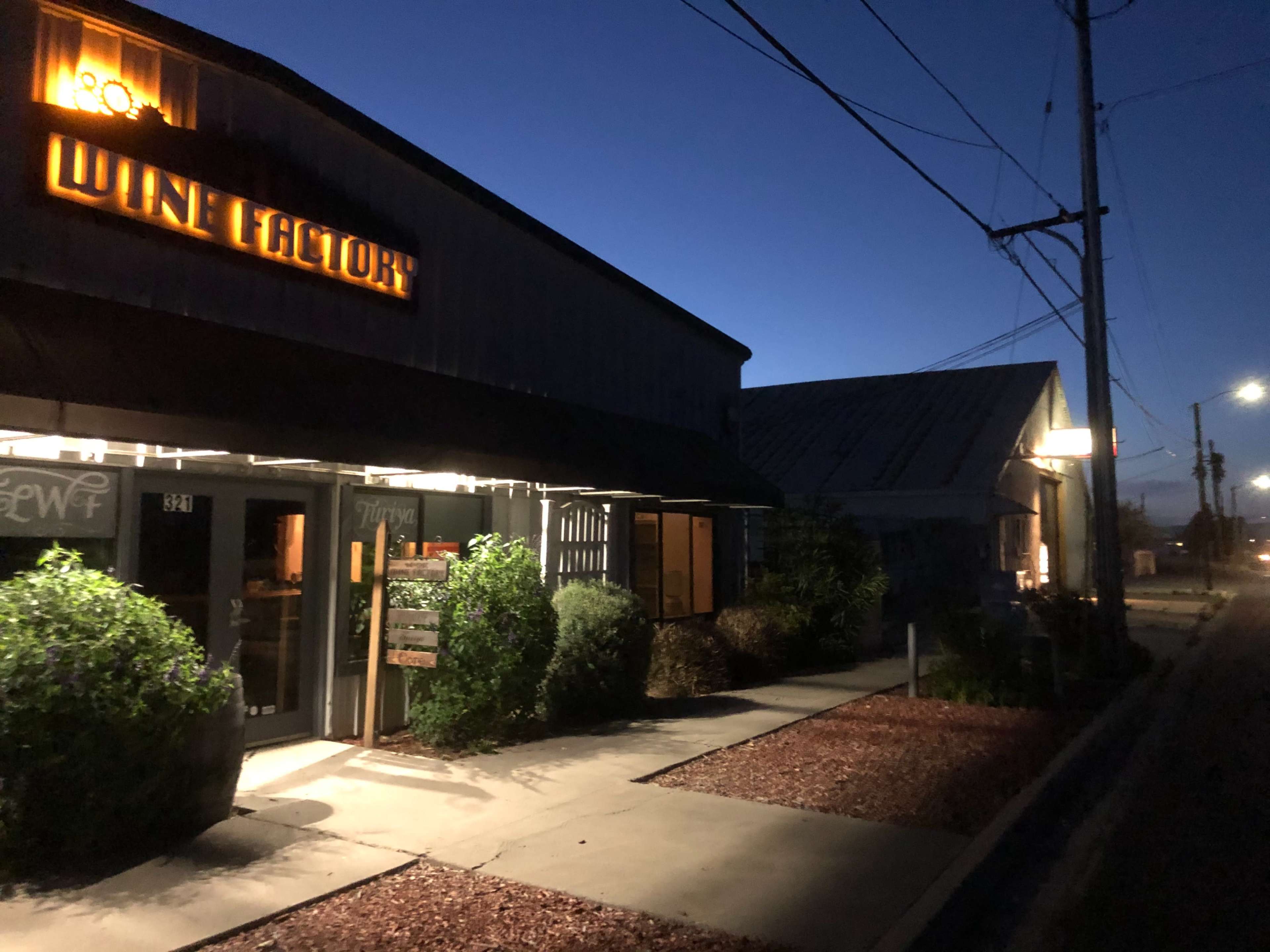A wine store with a lit sign, set against a twilight sky, along a street lined with power lines.