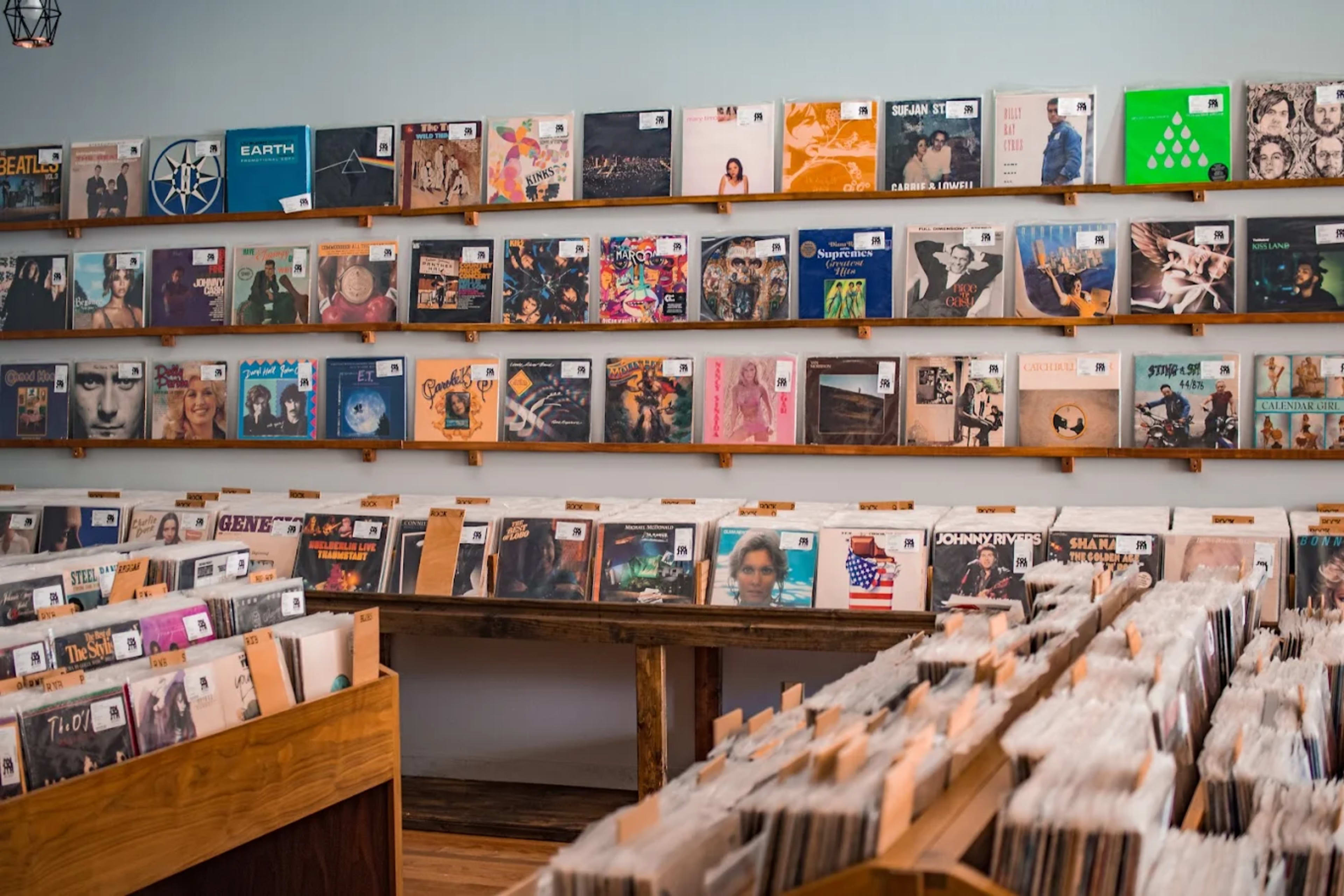 A record store displays rows of vinyl albums on the walls and wooden crates filled with records in the foreground.