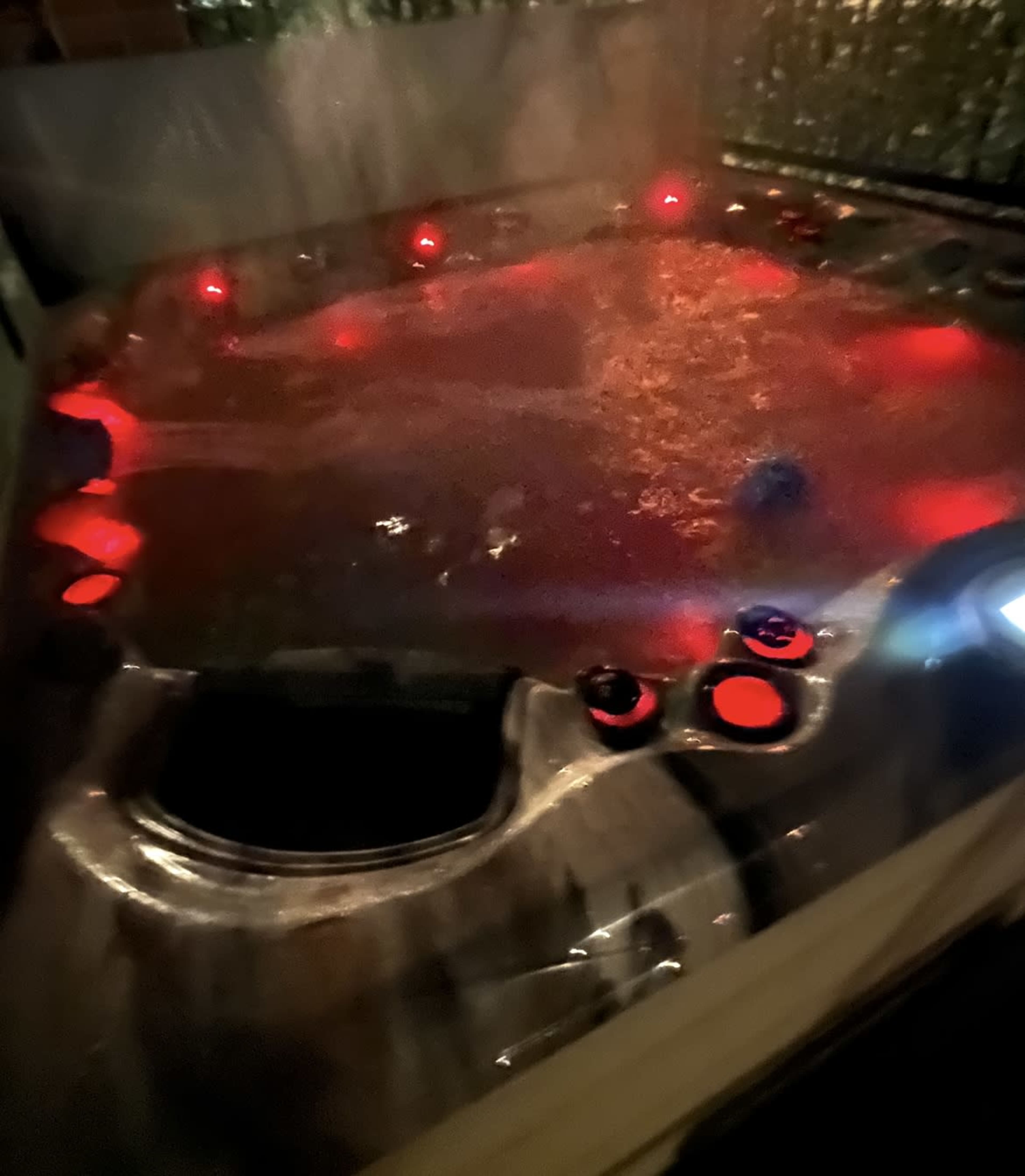 A hot tub filled with water and illuminated by red lights is positioned in a dimly lit area.