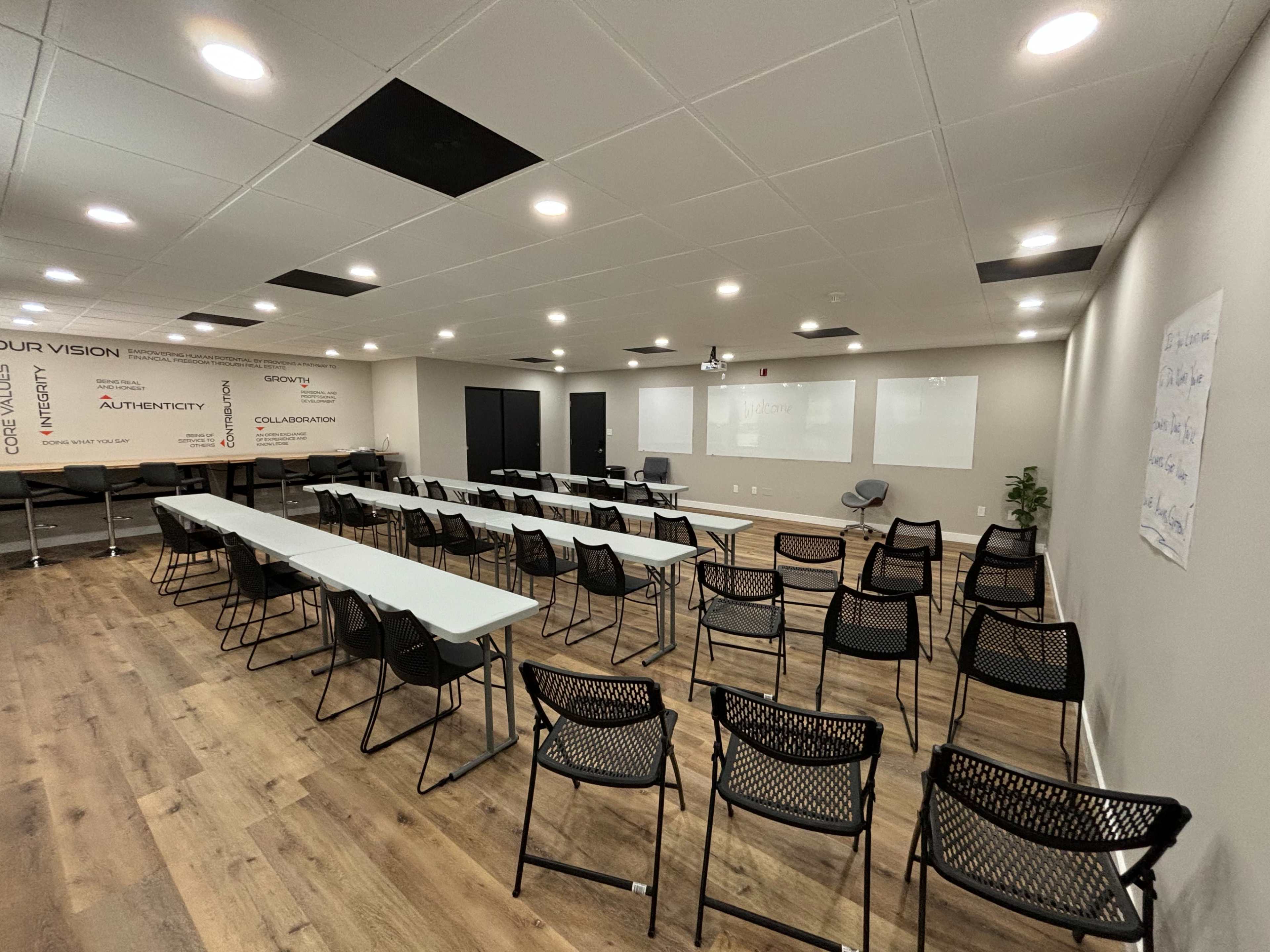 A conference room is set up with several rows of chairs facing a projector screen, flanked by white walls featuring inspirational phrases.