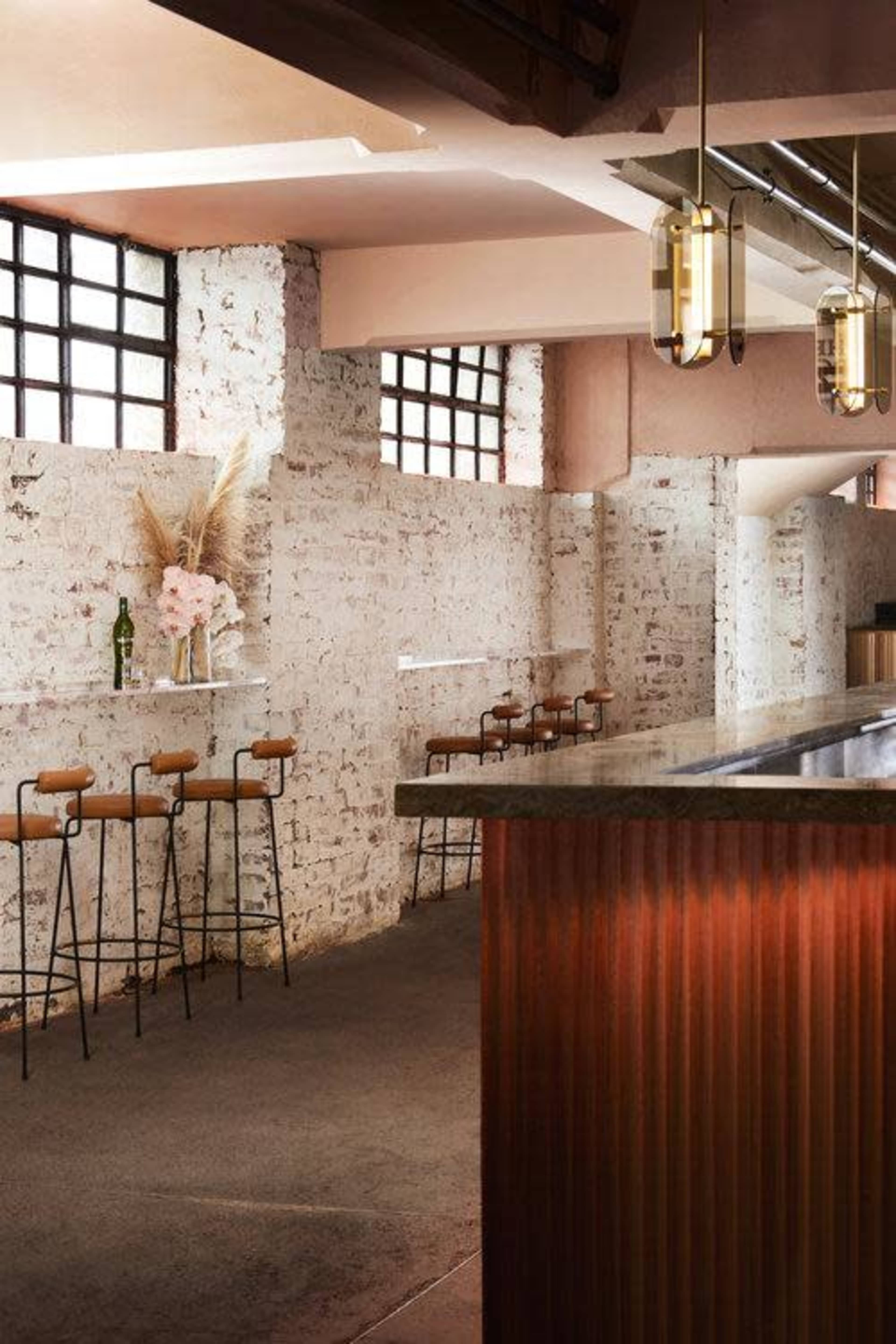 A modern bar area with high stools along a brick wall and a polished countertop, illuminated by contemporary pendant lights.