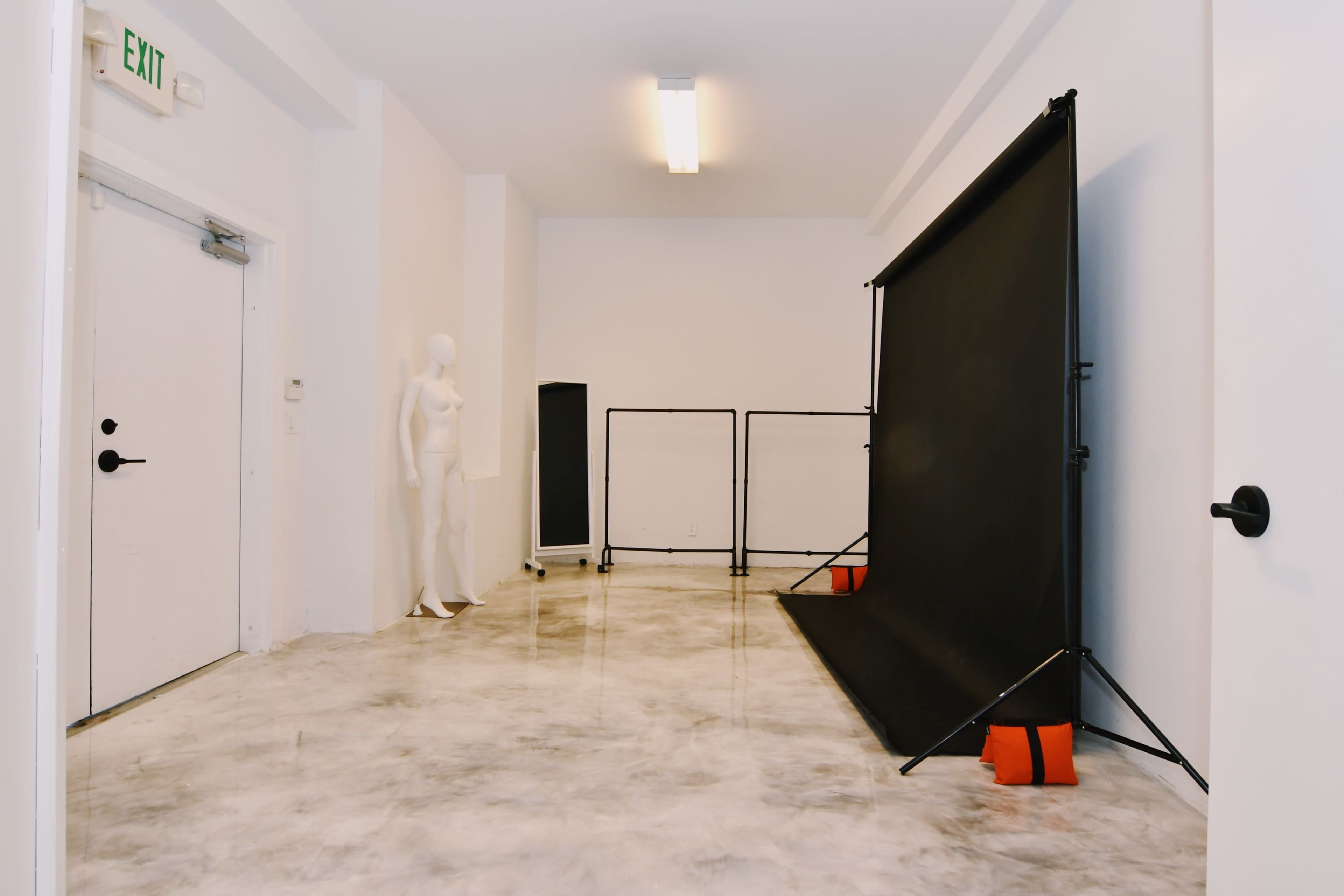 A spacious room with a glossy floor features a black backdrop on stands, a clothing rack, a mannequin, and a door.