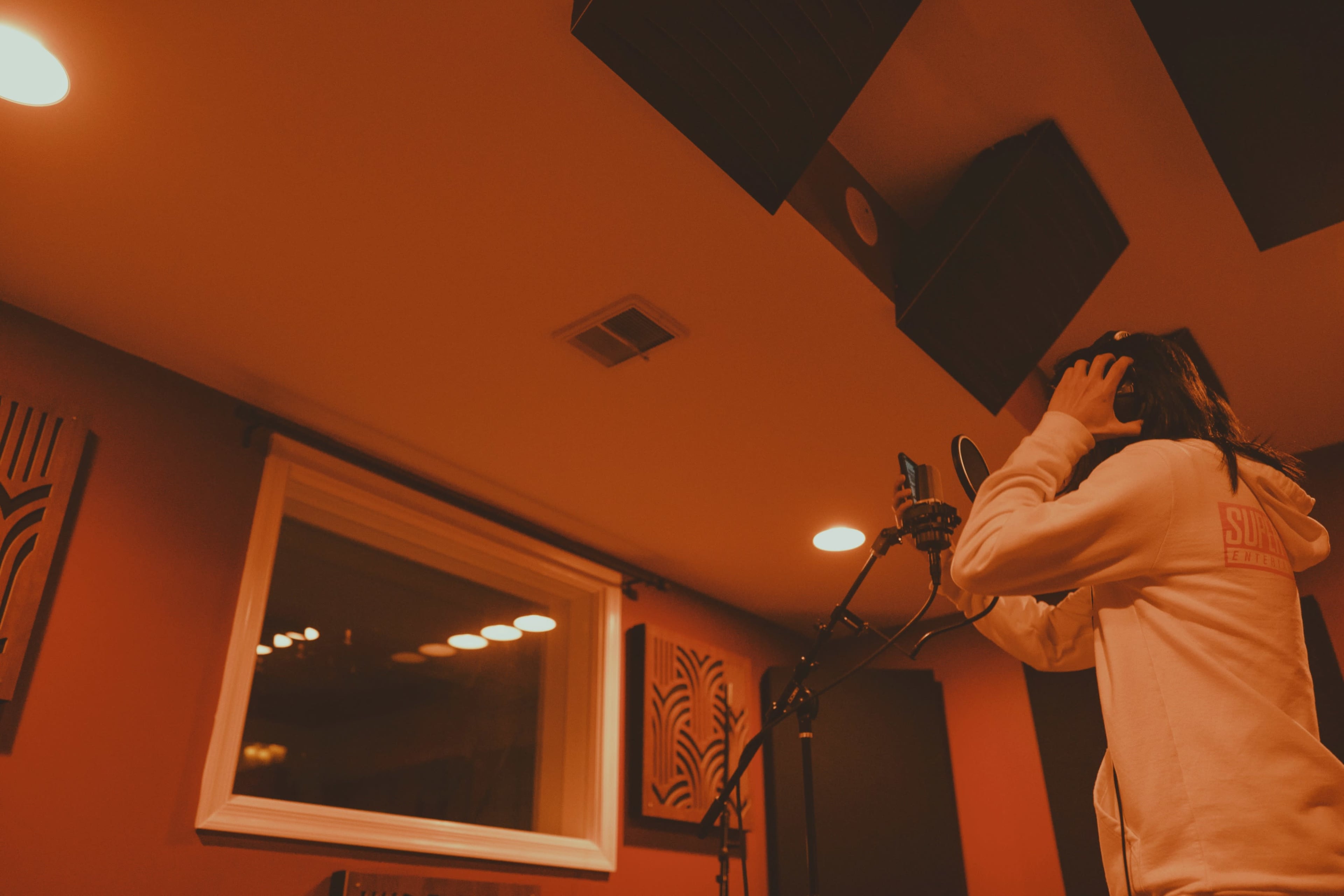 A person stands in a recording studio, wearing headphones while singing into a microphone.