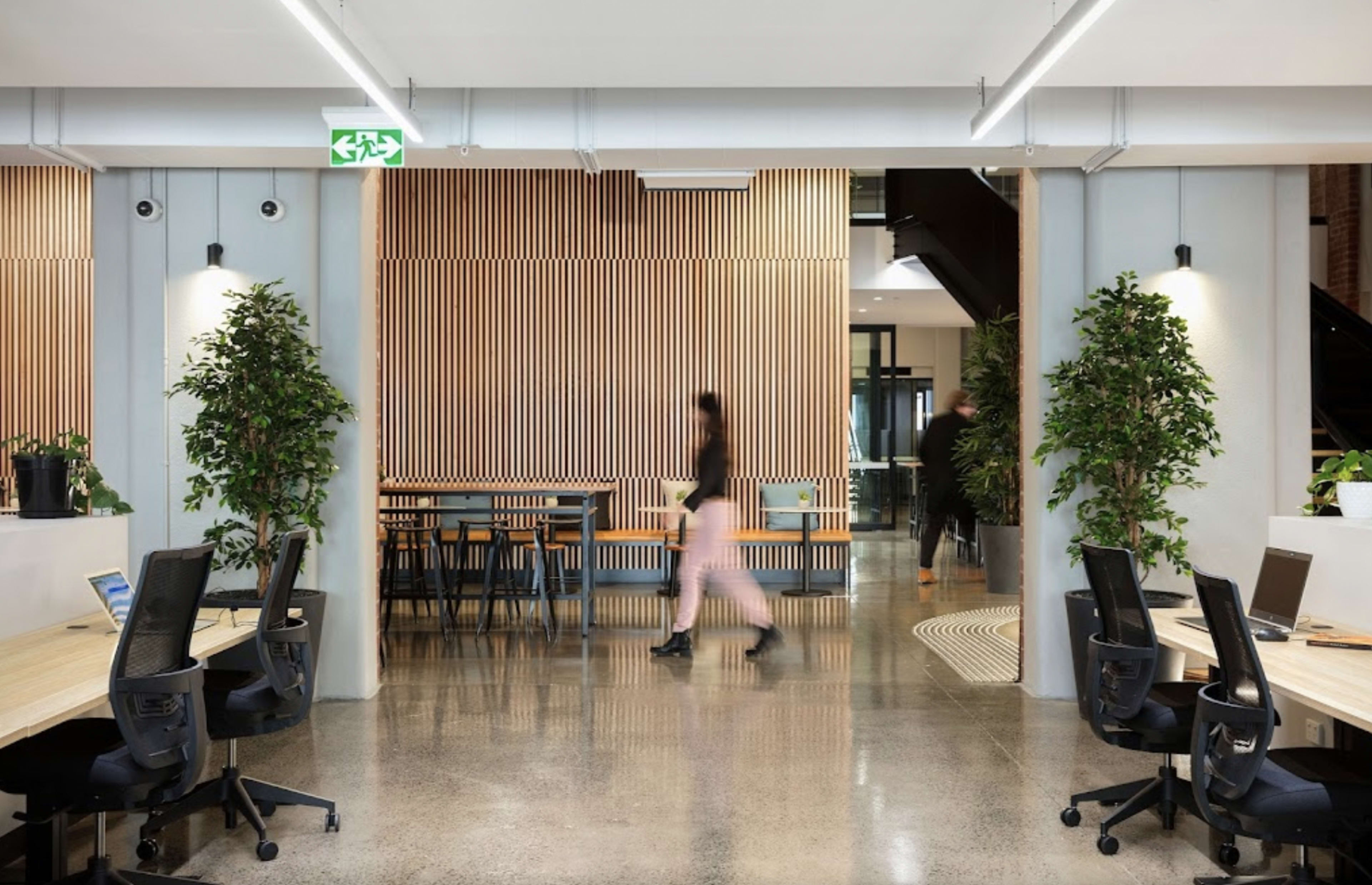 A modern office space features wooden paneling, plants, and a layout that includes desks and a dining area.