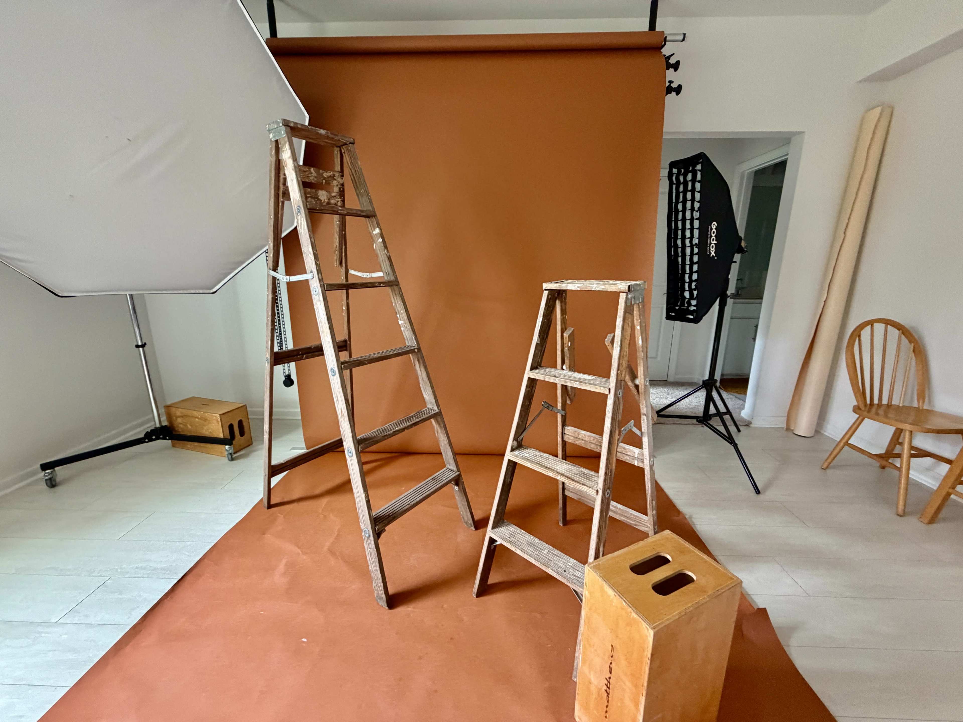The image shows two wooden ladders positioned on a brown backdrop in a photography studio.