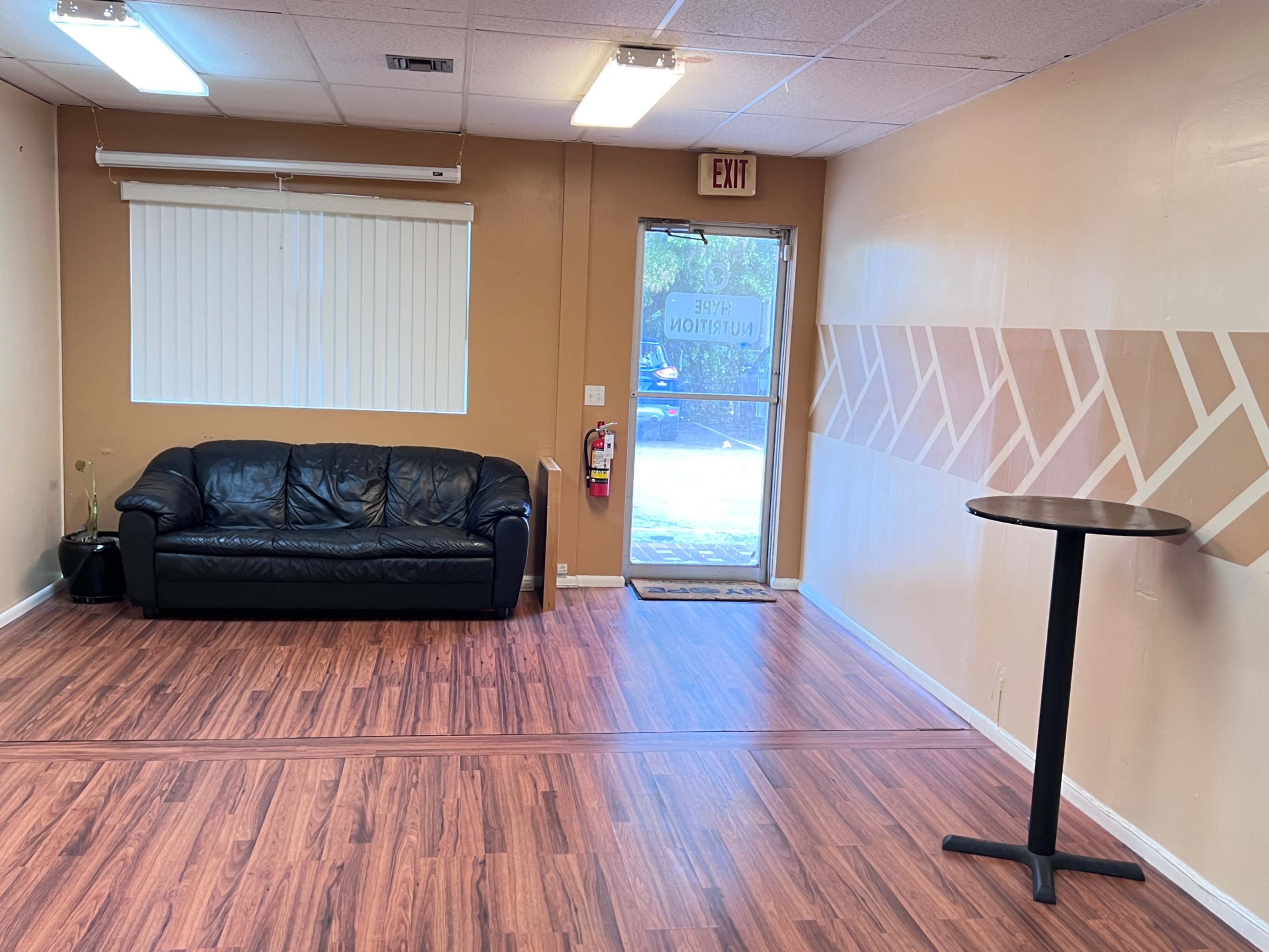 A room with a black leather couch, a small round table, and a door leading outside.