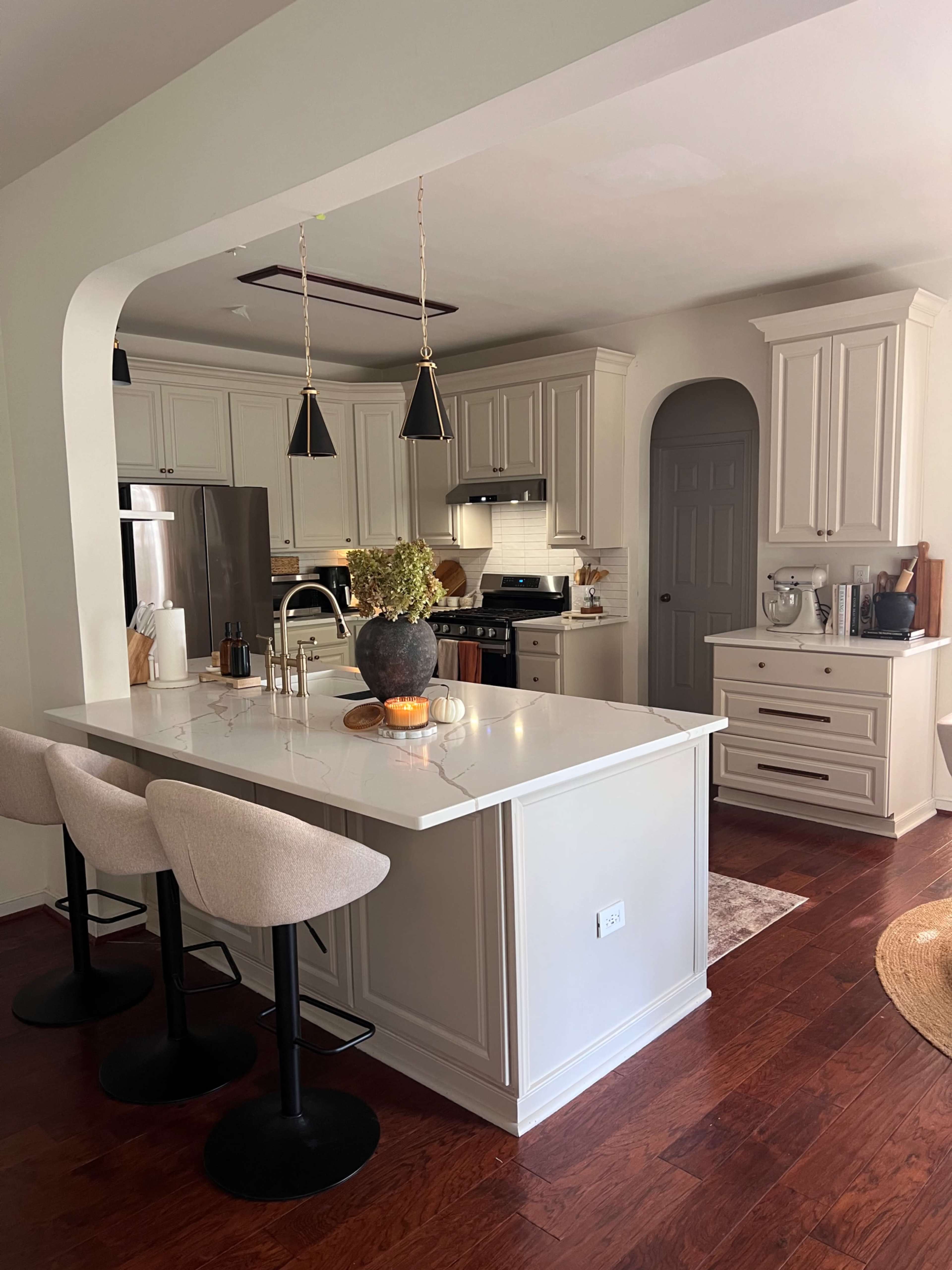 The image shows a modern kitchen with light cabinetry, an island with bar stools, and stainless steel appliances.