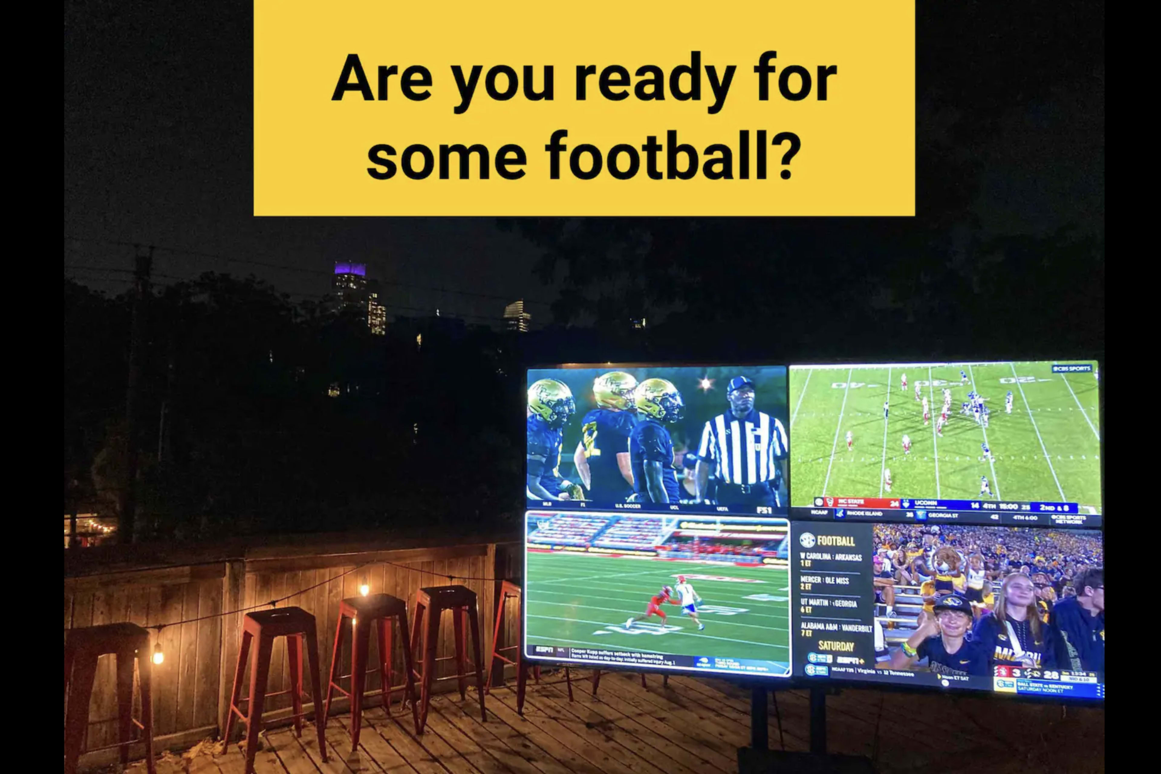 A large outdoor screen displays a football game, accompanied by seating and city lights in the background.