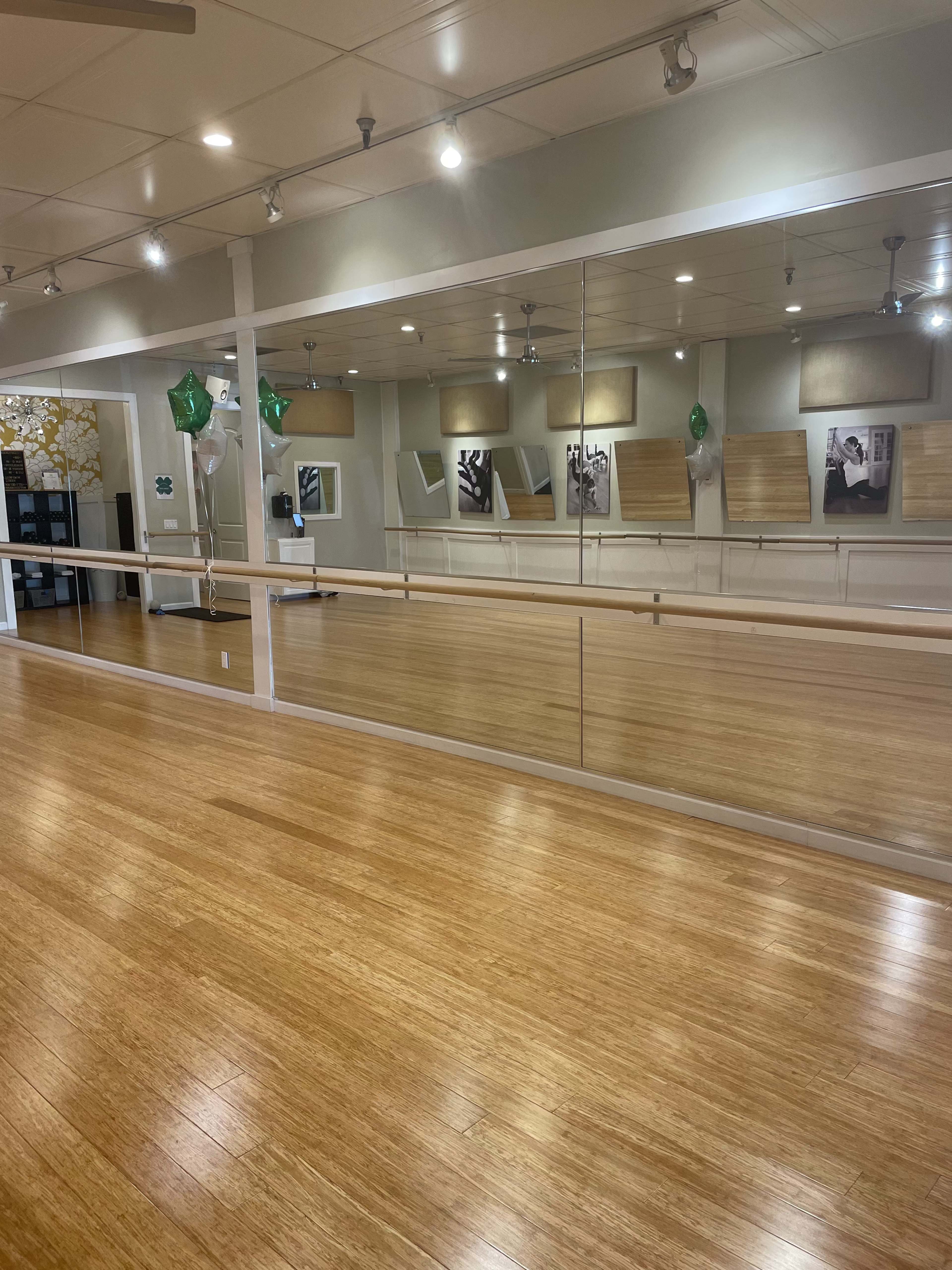 A spacious dance studio with wooden flooring, large mirrors, artwork on the walls, and green balloons.